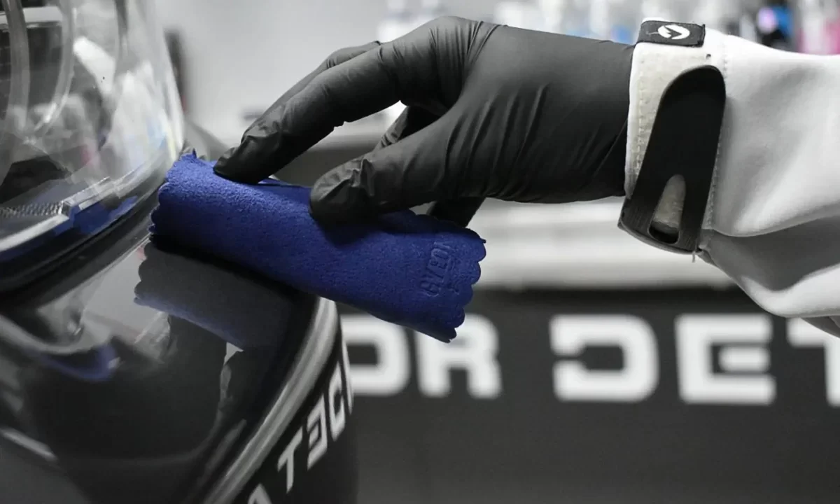 A person wearing a black glove cleaning a black surface with a blue microfiber cloth.