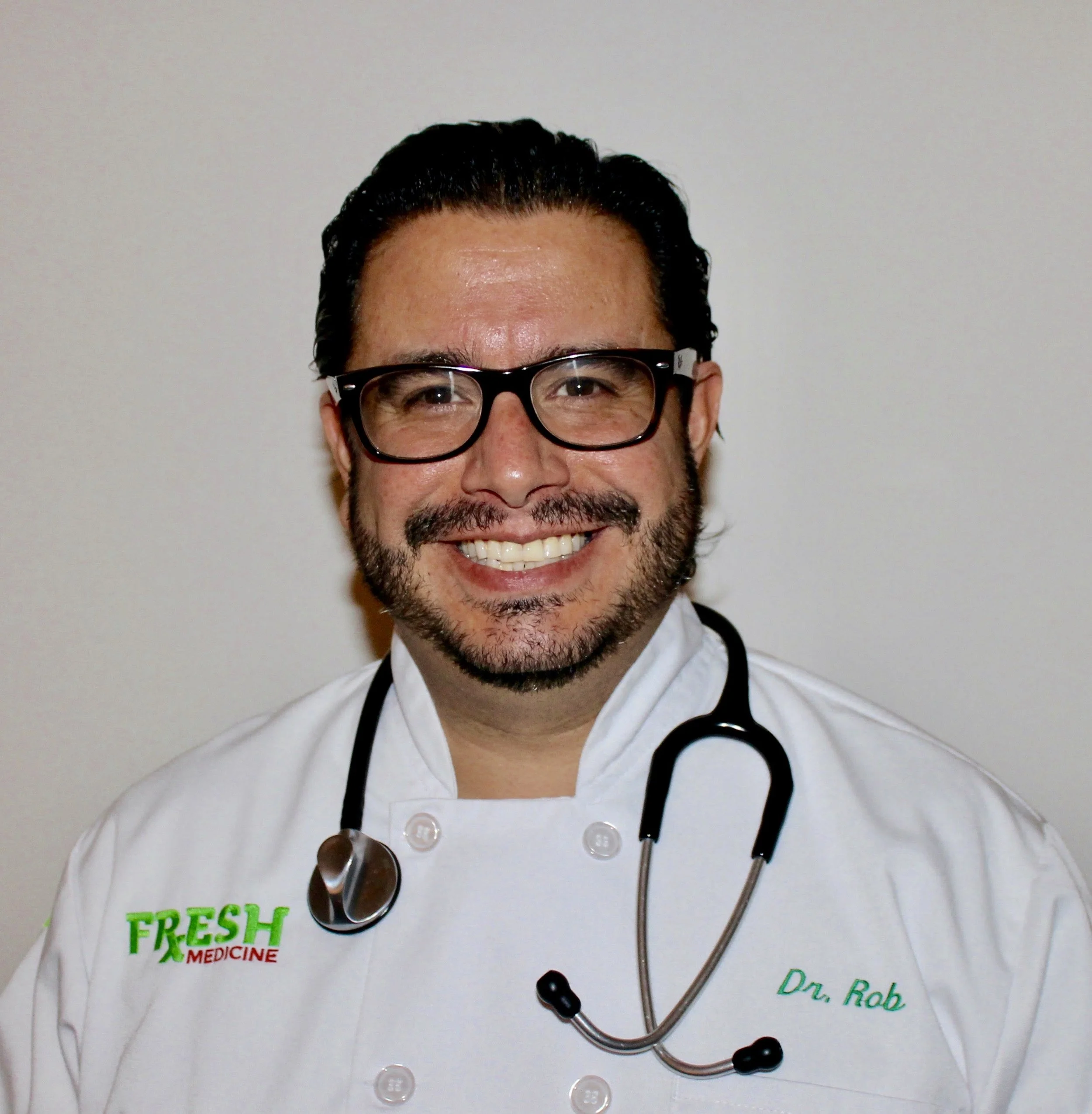 Smiling male doctor wearing glasses, white coat with 'FRESH MEDICINE' embroidered, stethoscope around neck, named Dr. Rob, against plain background.