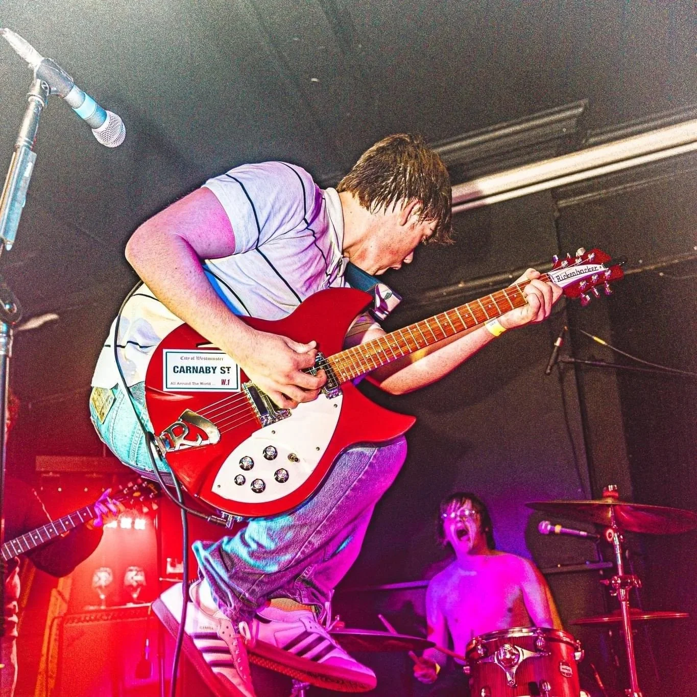 Finn Sexton jumping on stage with Denny Keil in the background on drums playing with Monumental