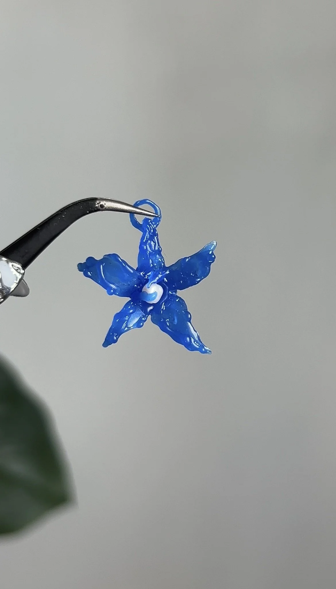 A blue flower-shaped dental crown or veneer held by dental tweezers against a plain background.