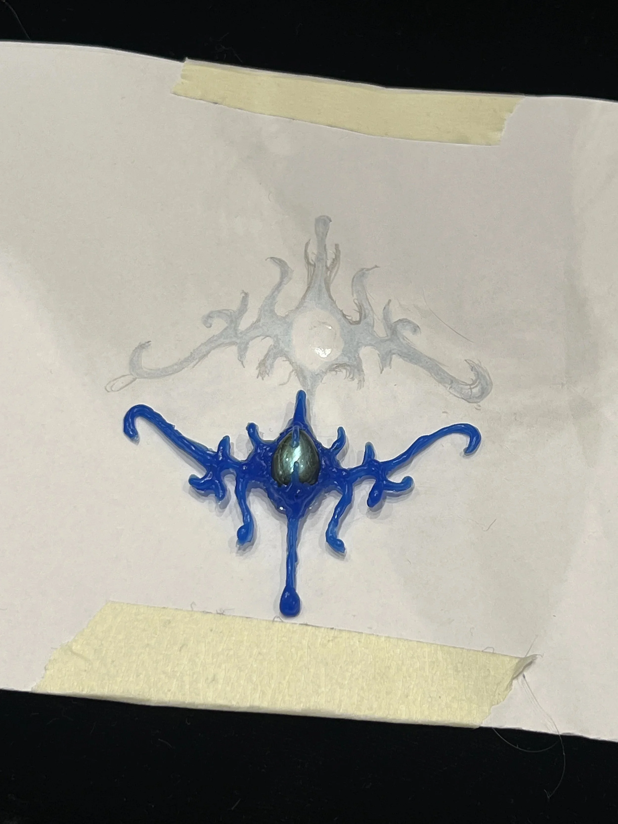 A baseball with blue and black paint drip design on white paper, taped at the top and bottom.