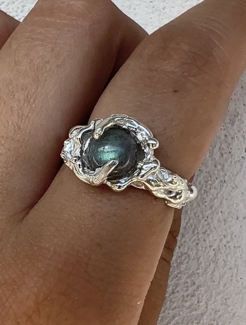 Close-up of a silver ring with a large, dark, shiny gemstone on a person's finger.