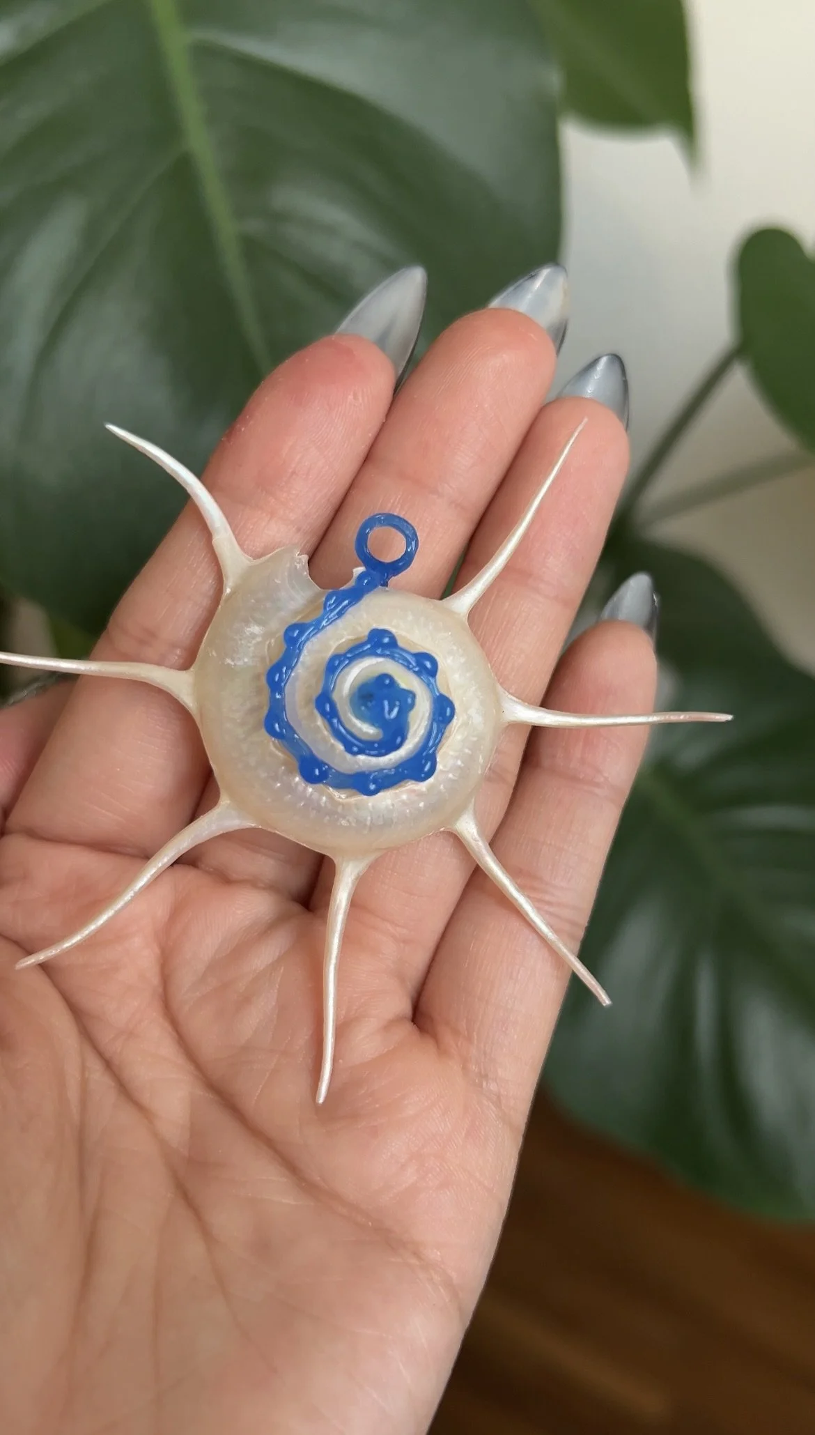 A decorative glass ornament resembling a sea creature with a spiral pattern in the center, multiple extending spines, and blue painted details.