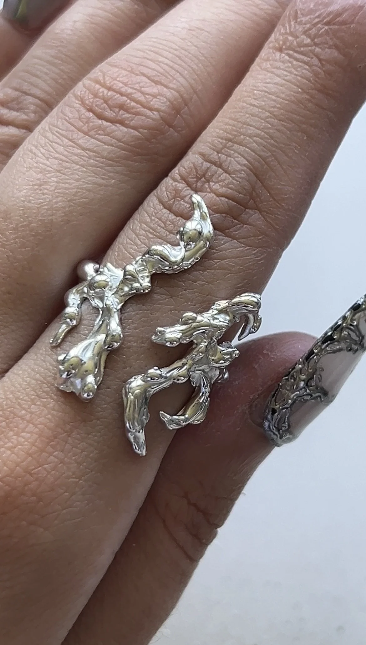 Close-up of a hand wearing a silver ring designed to look like two intertwined sea horses.