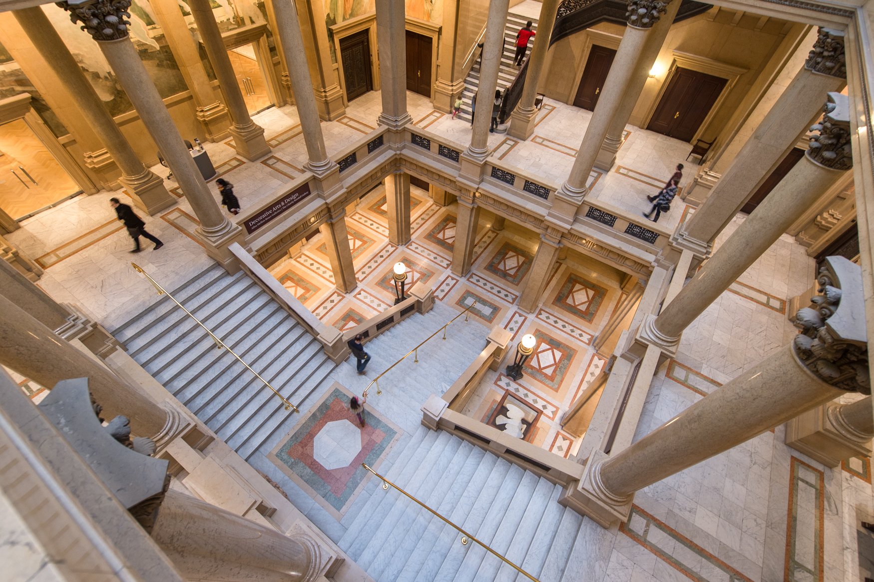 An overhead shot of the grand staircase at the Carnegie Museum of Art, featuring multiple levels of stairs flanked by floor-to-ceiling Corinthian columns