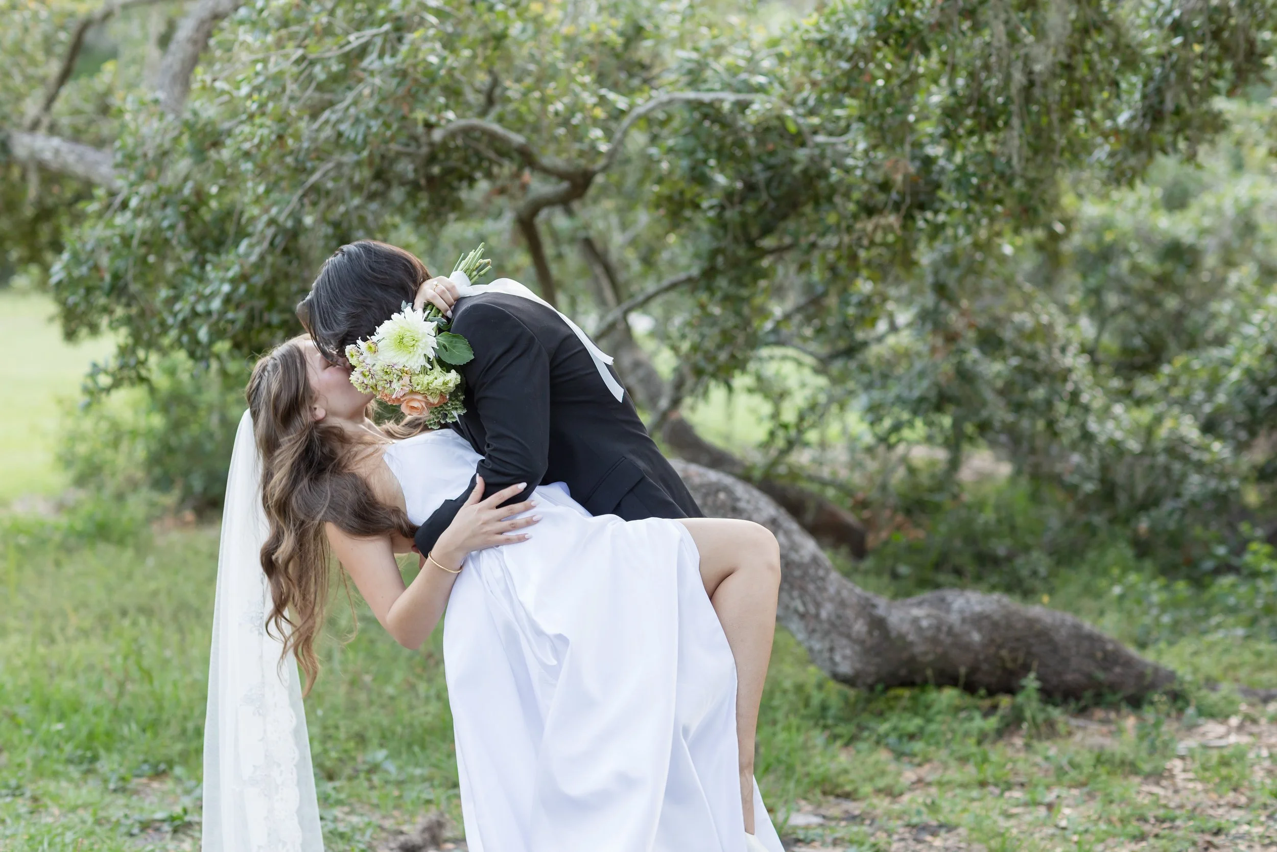 Romantic dip kiss beneath mossy oaks during an outdoor Florida wedding