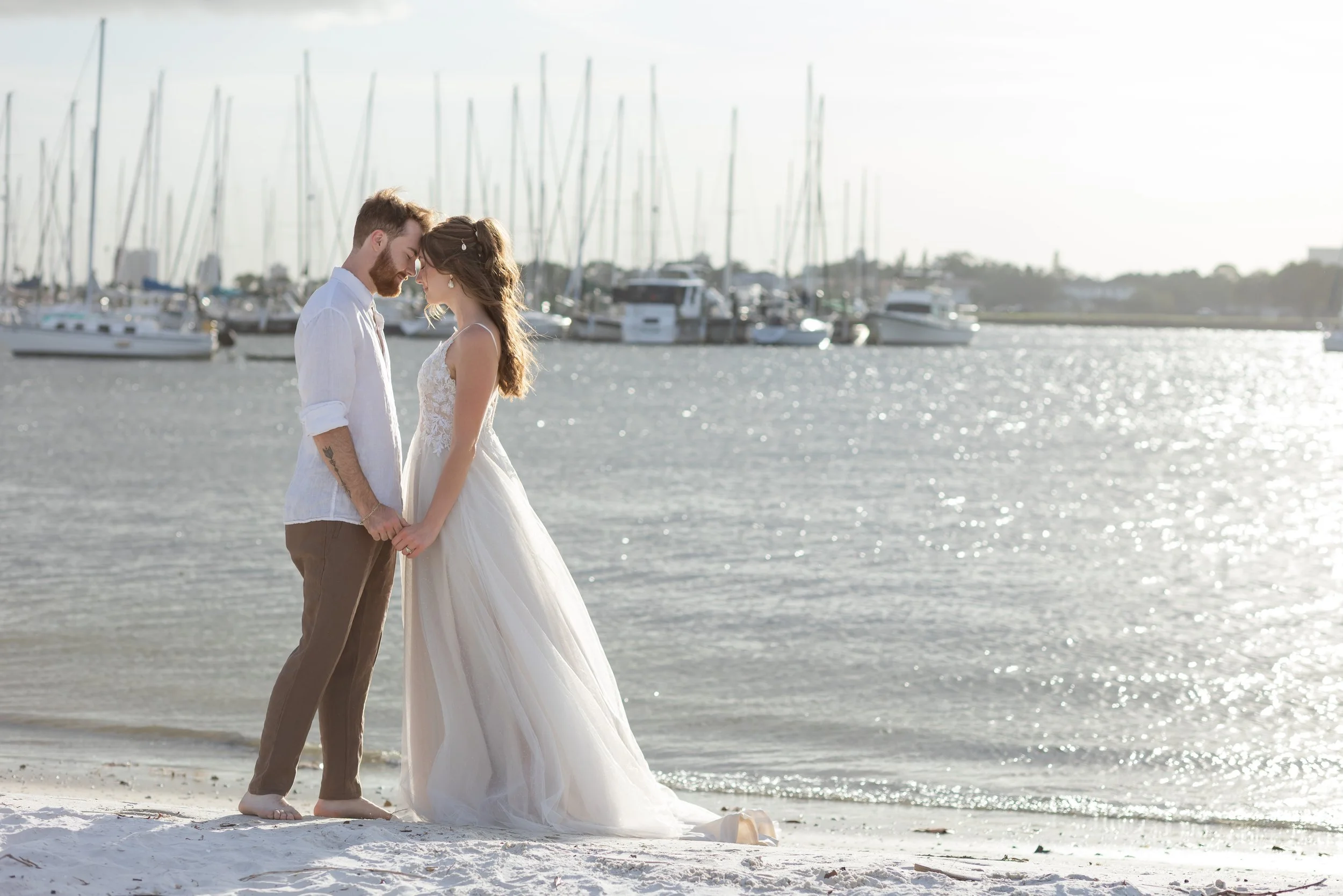 Newlyweds share a private moment on the white sand with sailboats in the distance at their Florida coastal elopement.