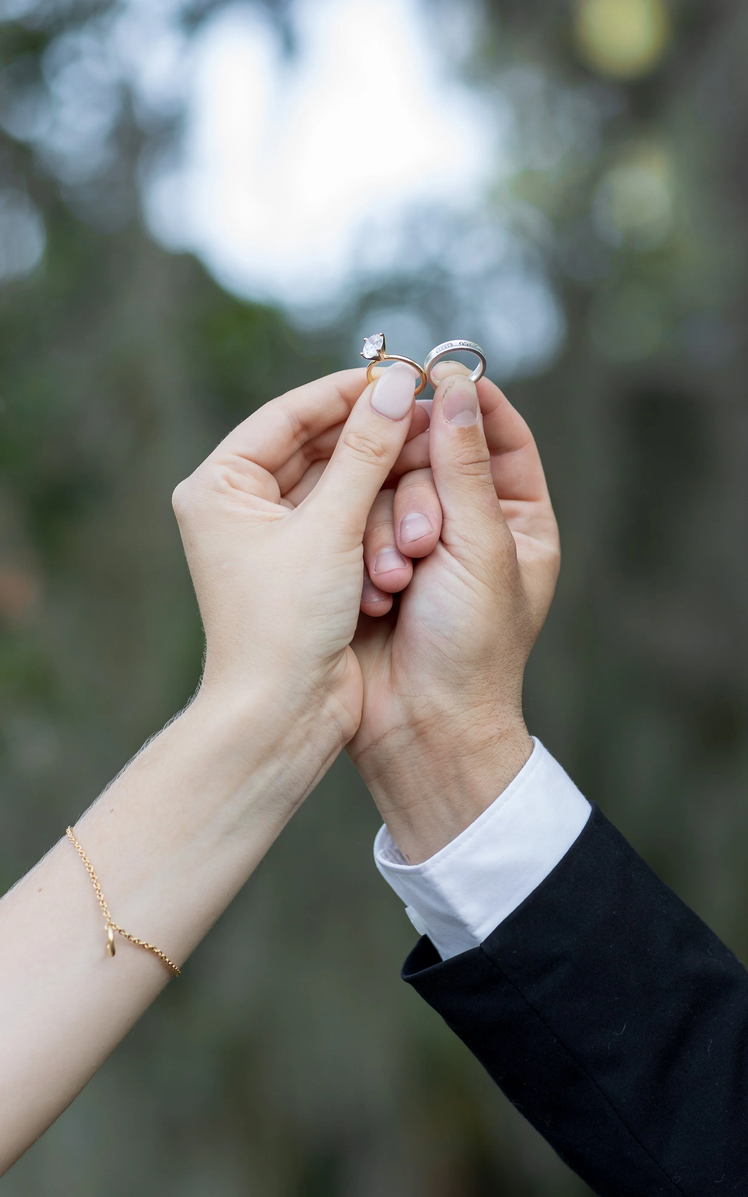 Close-up of couple’s hands holding wedding rings together against a soft, blurred outdoor background. Minimalist and symbolic wedding photography capturing the essence of commitment and love.