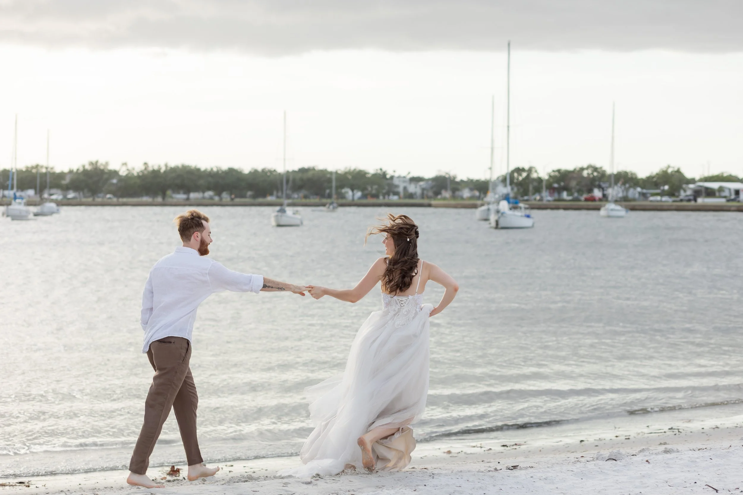Bride and groom run along the shoreline hand in hand during their playful post-elopement celebration in Tampa Bay.