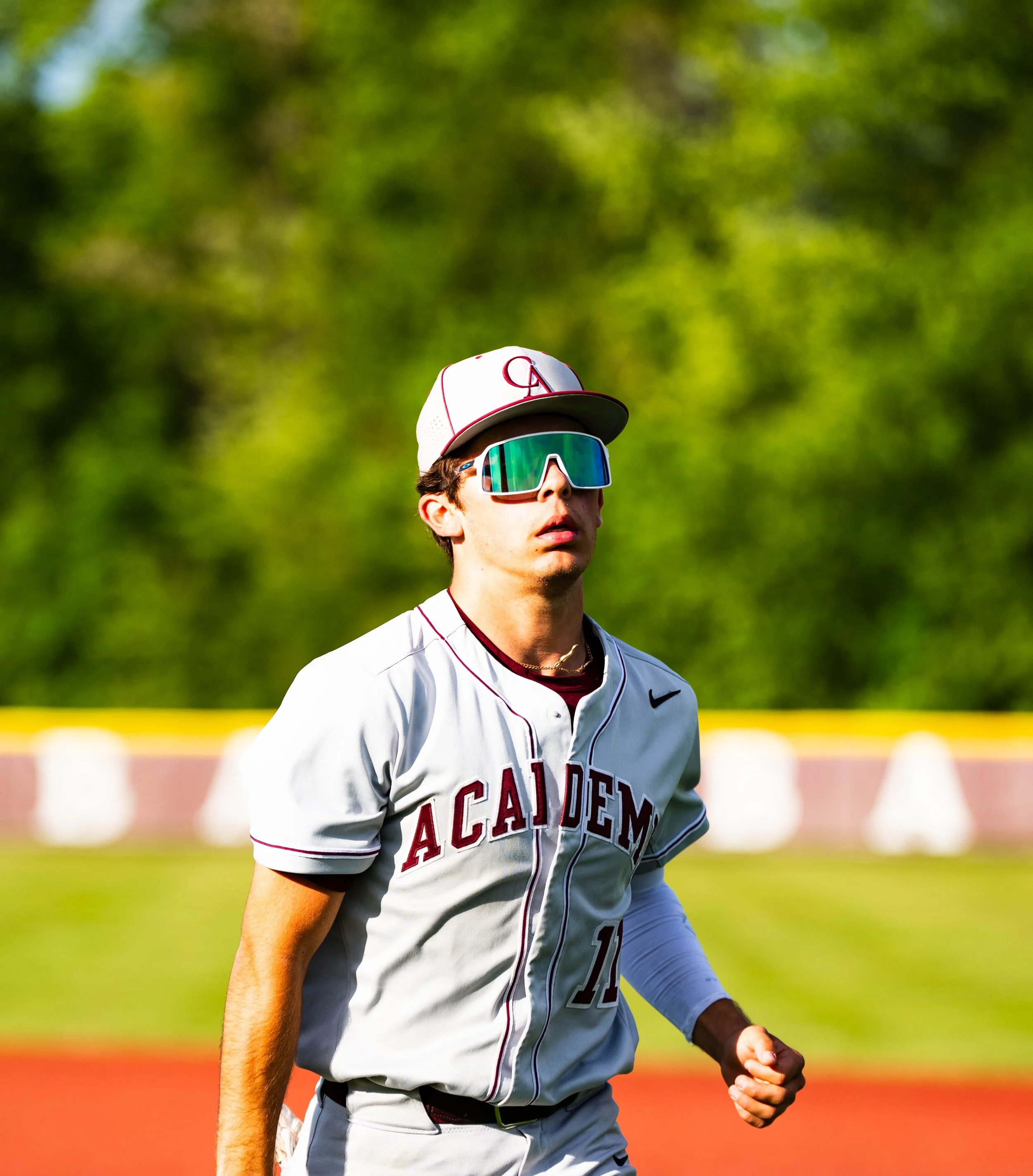 A baseball player wearing a white uniform with red lettering and a red and white cap, standing on a baseball field with a blurred green background.