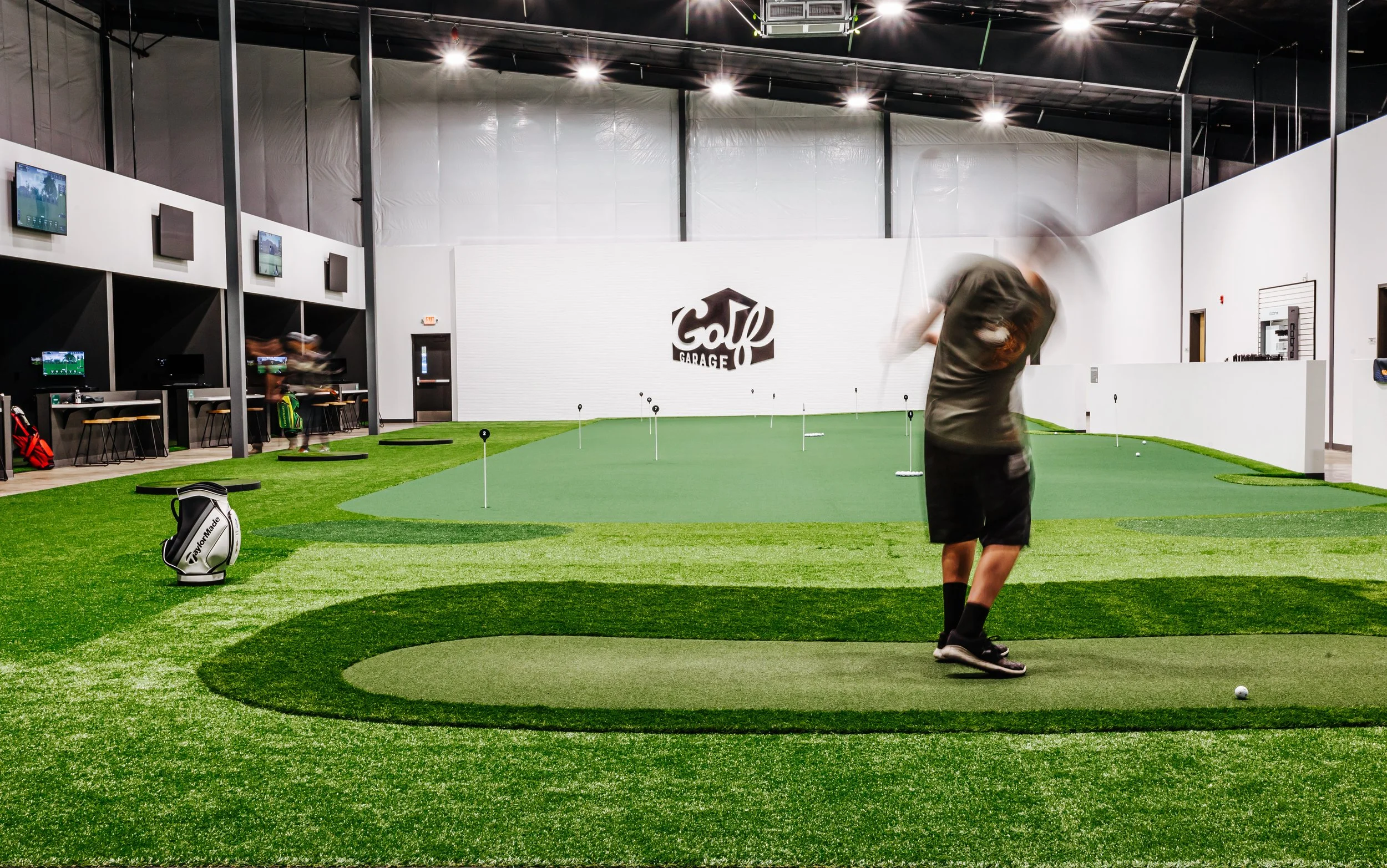 Indoor golf facility with putting greens and a person practicing their swing.