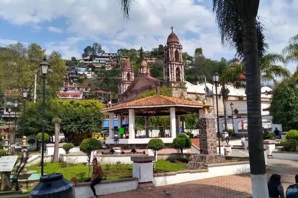 Public park with a gazebo, benches, trees, and a church with a bell tower in a hillside town.