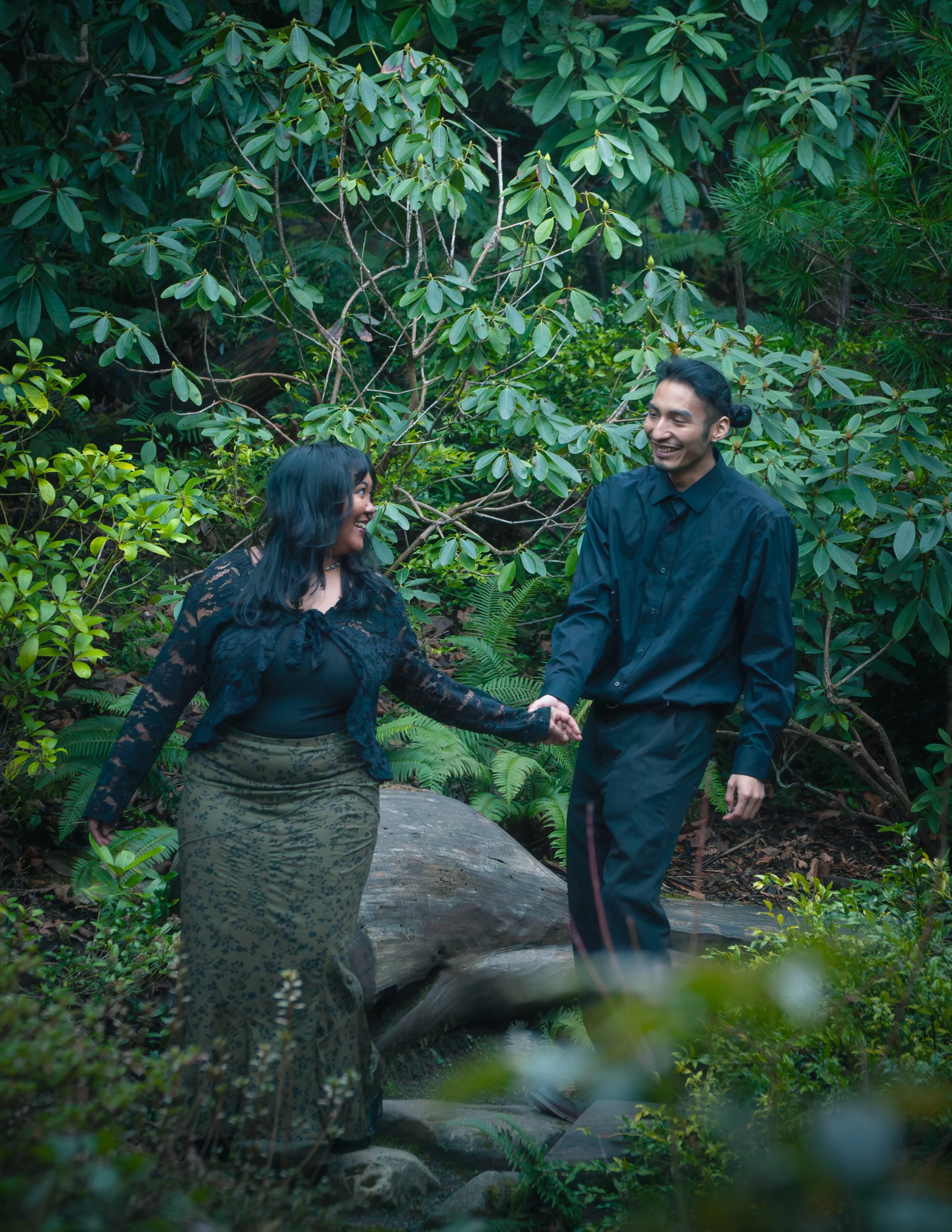 A man and woman holding hands and smiling in a lush green forest. in bellevue, Washington