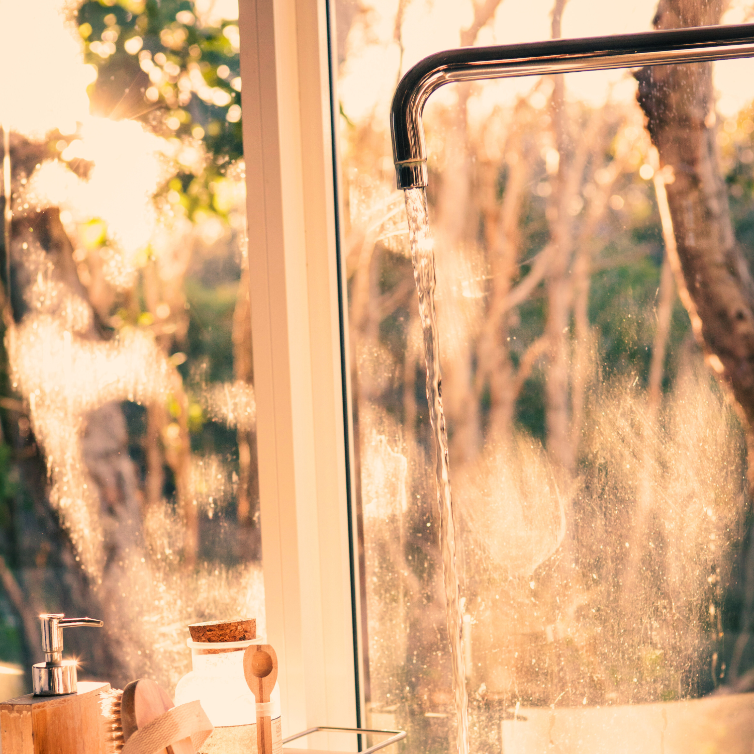 Sunlight streams through a window with a faucet pouring water, with outdoor trees visible through the foggy glass.