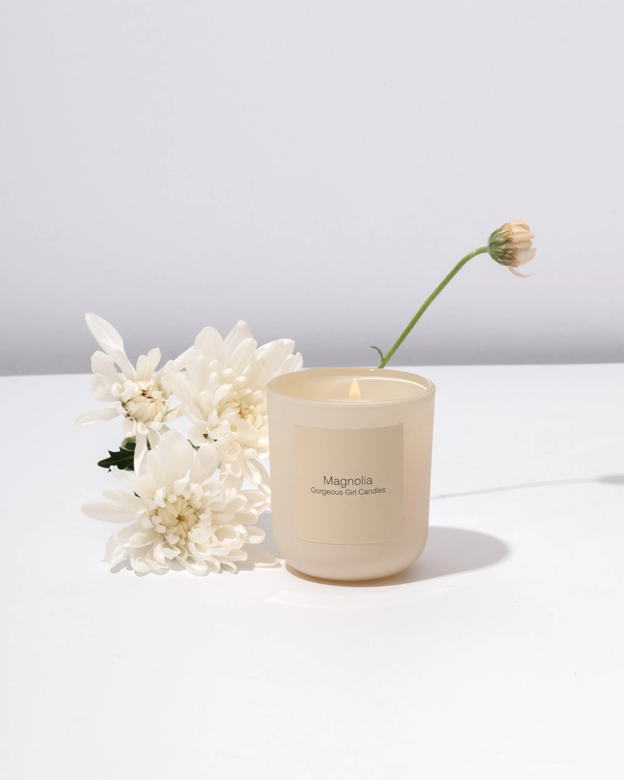 Still life product photography showcasing a magnolia scented candle styled with magnolia flowers.