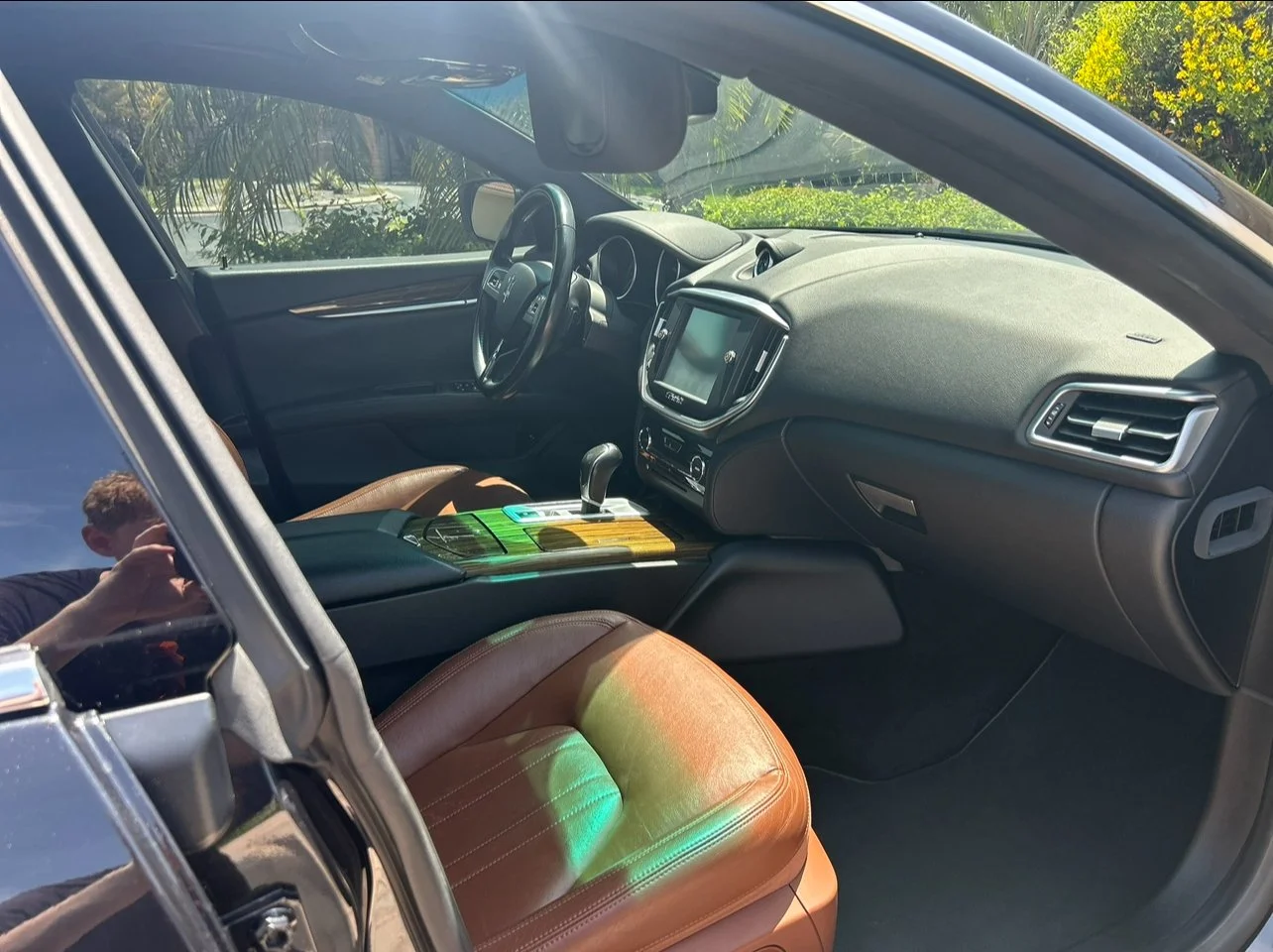 Interior of a modern car showing a black dashboard, steering wheel, gear shift, and brown leather seat with sunlight streaming in.