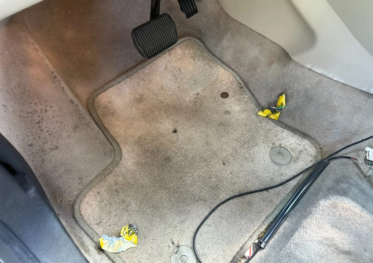 Dirty car floor mat with two candy wrappers and some loose wires.