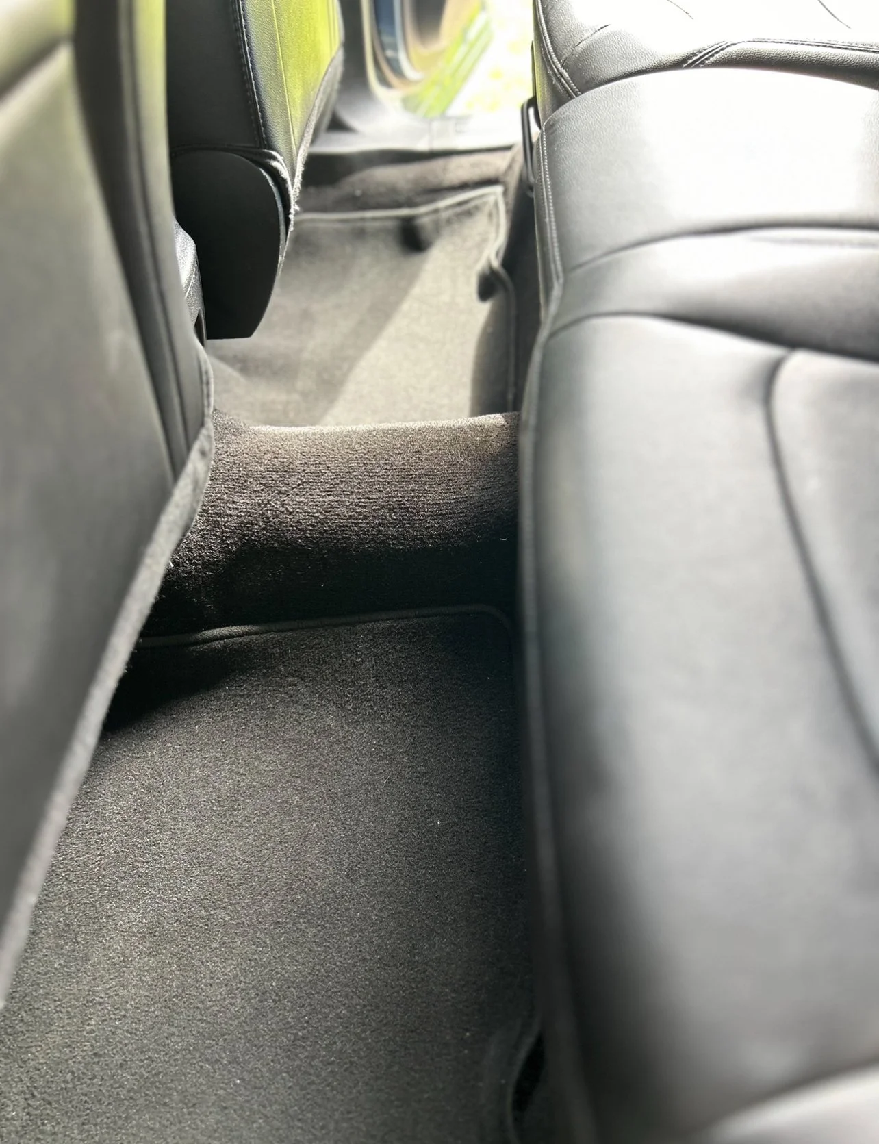 View of the backseat interior of a car, showing carpeted floor and black leather seats.
