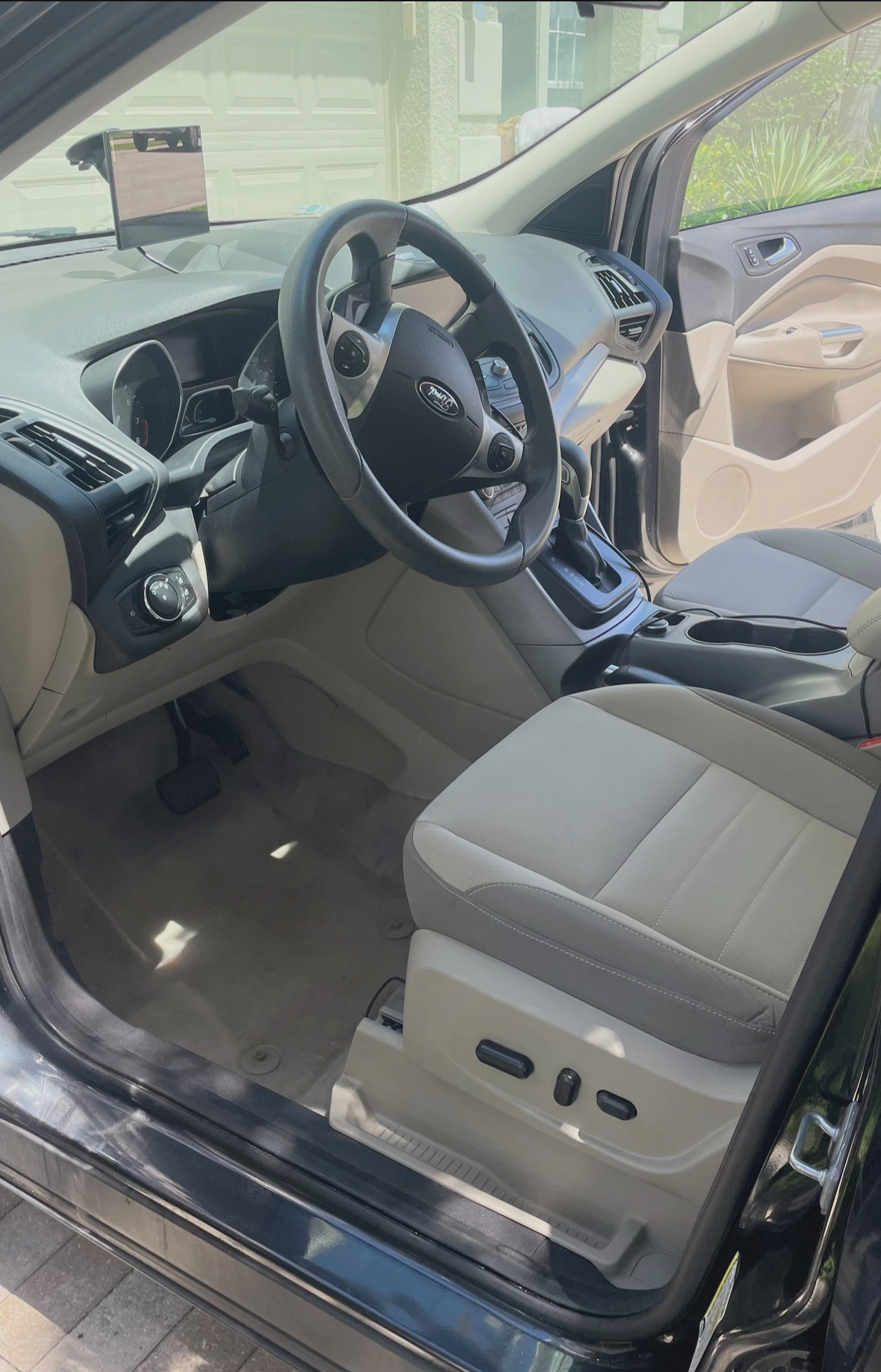 Interior of a Ford vehicle with a beige and gray color scheme, showing the steering wheel, gear shift, dashboard, and front passenger seat.
