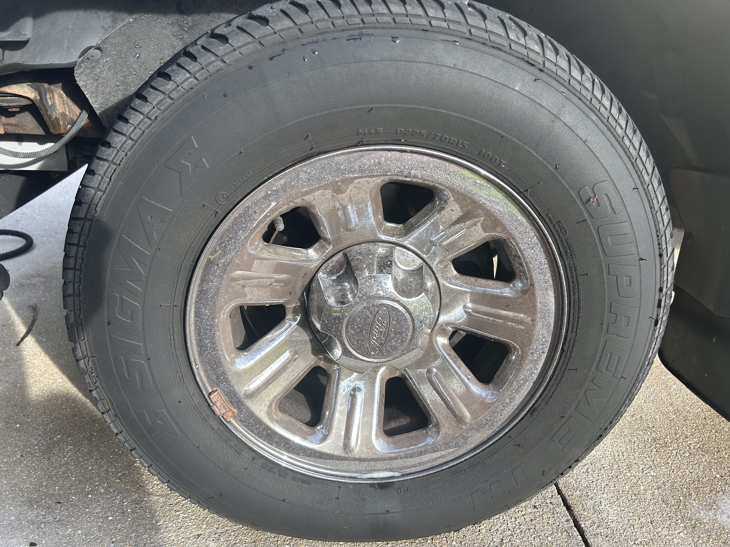 A vehicle tire with a chrome rim and visible hubcap, mounted on a car, on a concrete surface.