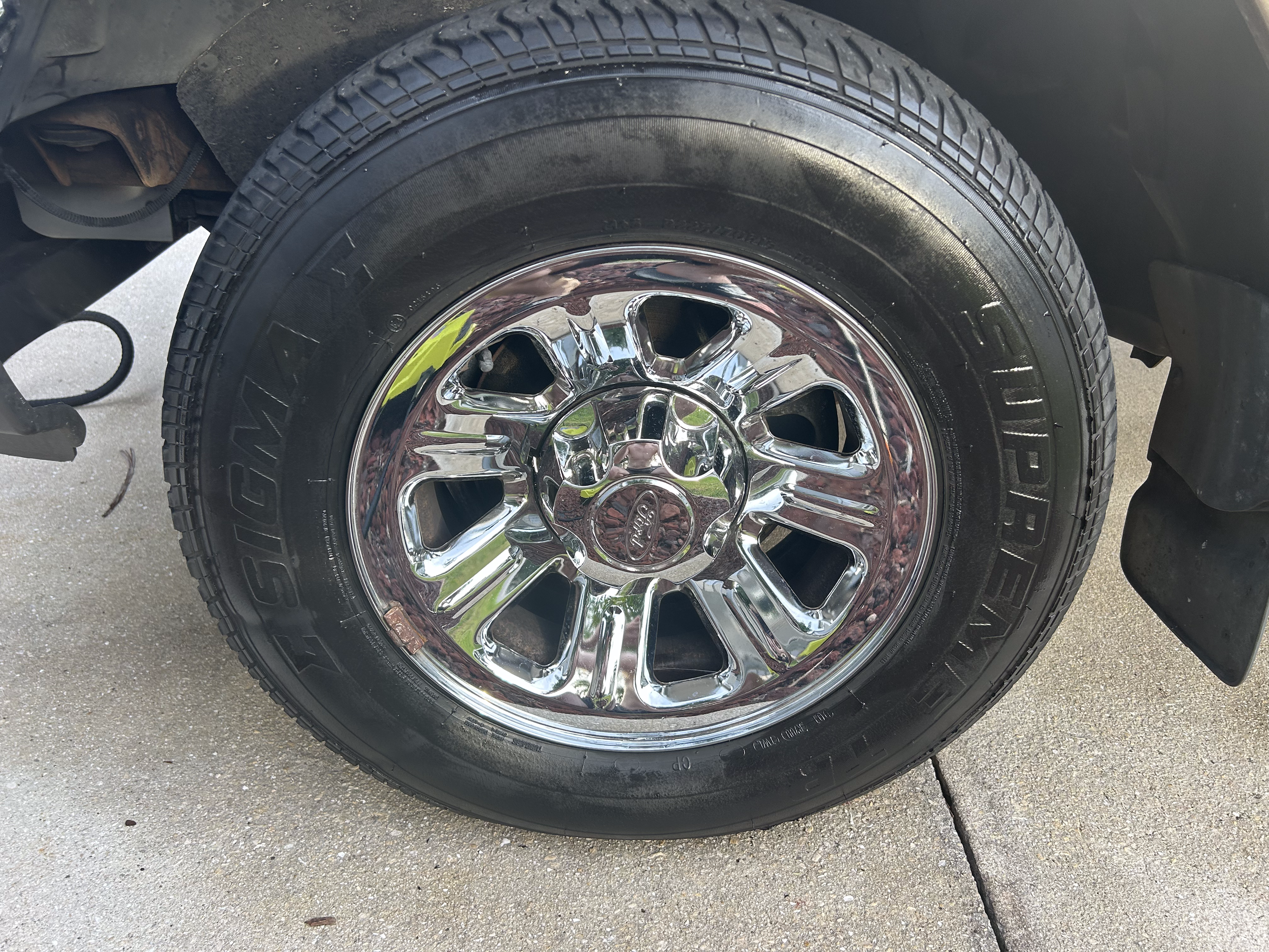 Close-up of a car tire with a shiny chrome wheel on a concrete driveway.