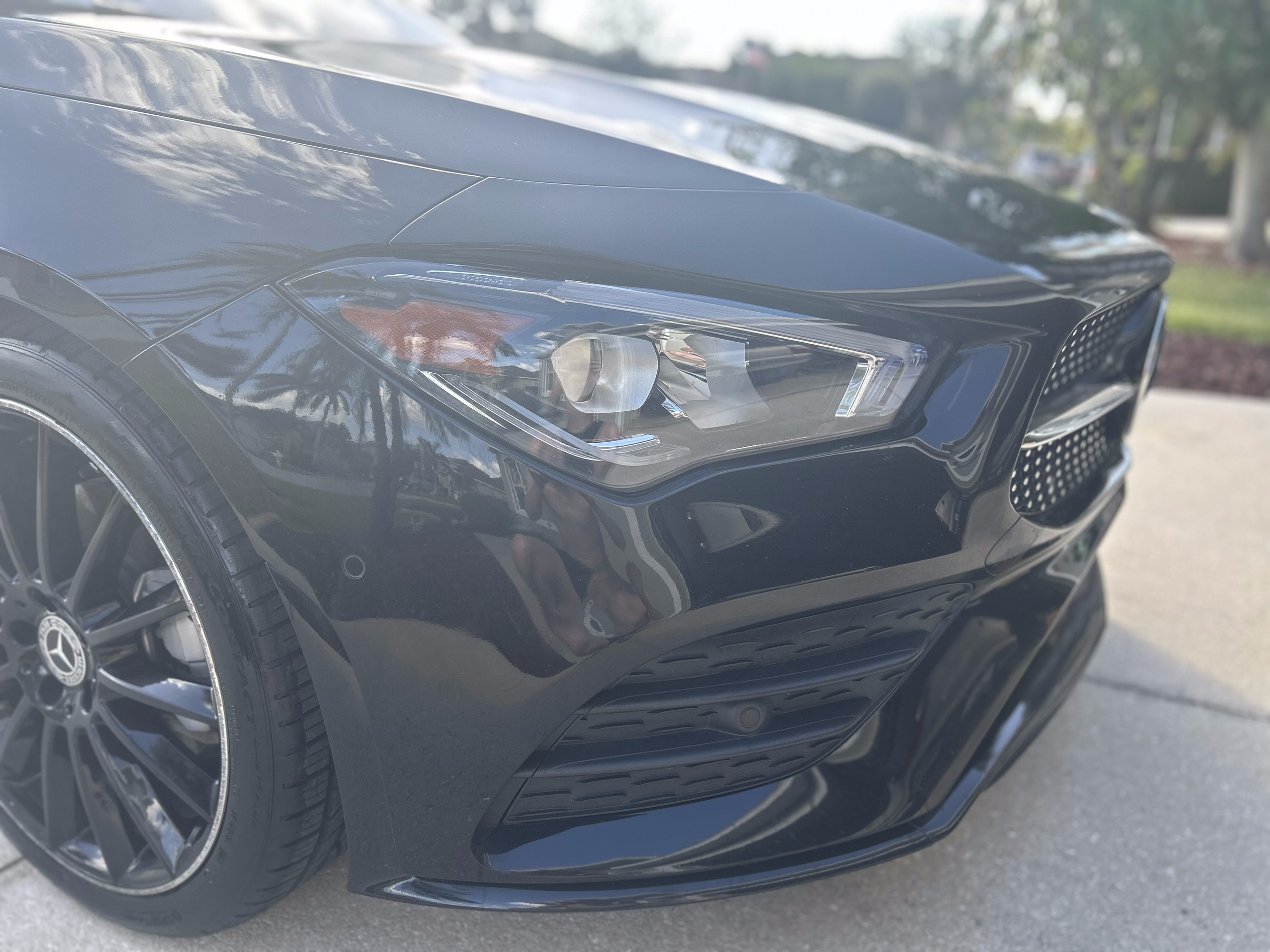 Close-up of the front left side of a black Mercedes-Benz car, showing the headlight, wheel, and front grille.