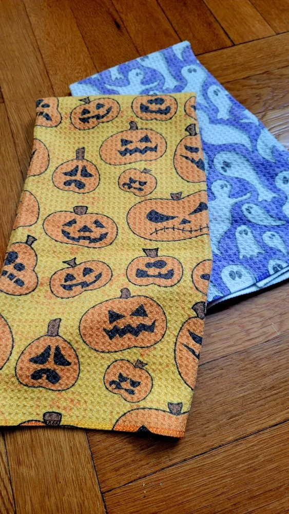 Two Halloween tea towels featuring jack-o-lantern pumpkins and ghosts