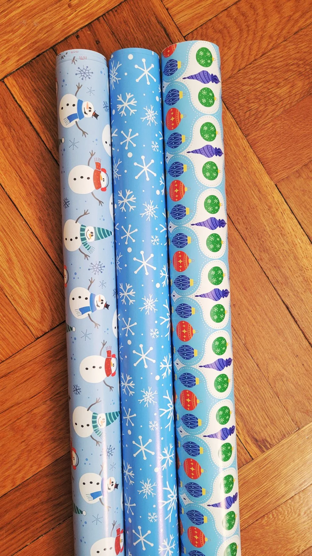Three rolls of holiday wrapping paper featuring snowmen, snowflakes, and Christmas ornaments