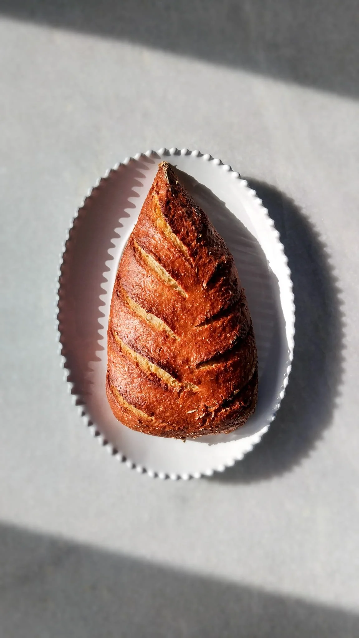 VECETO: Sourdough scored in pine form, resting on a white plate on marble.