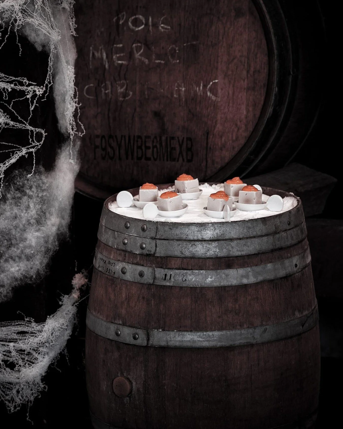 VECETO: Sensory excavation, cauliflower cubes on a salt-covered wine barrel. An apricot drop on each, black ground behind.