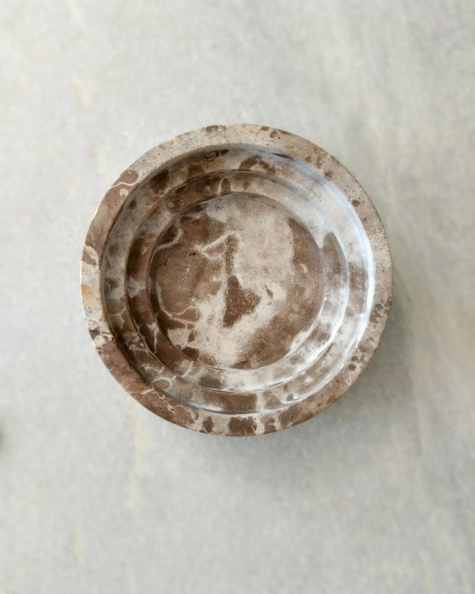 VECETO: Culinary trompe l'oeil, source of the grain. Brown and cream marble dish with stepped rim, seen from above.