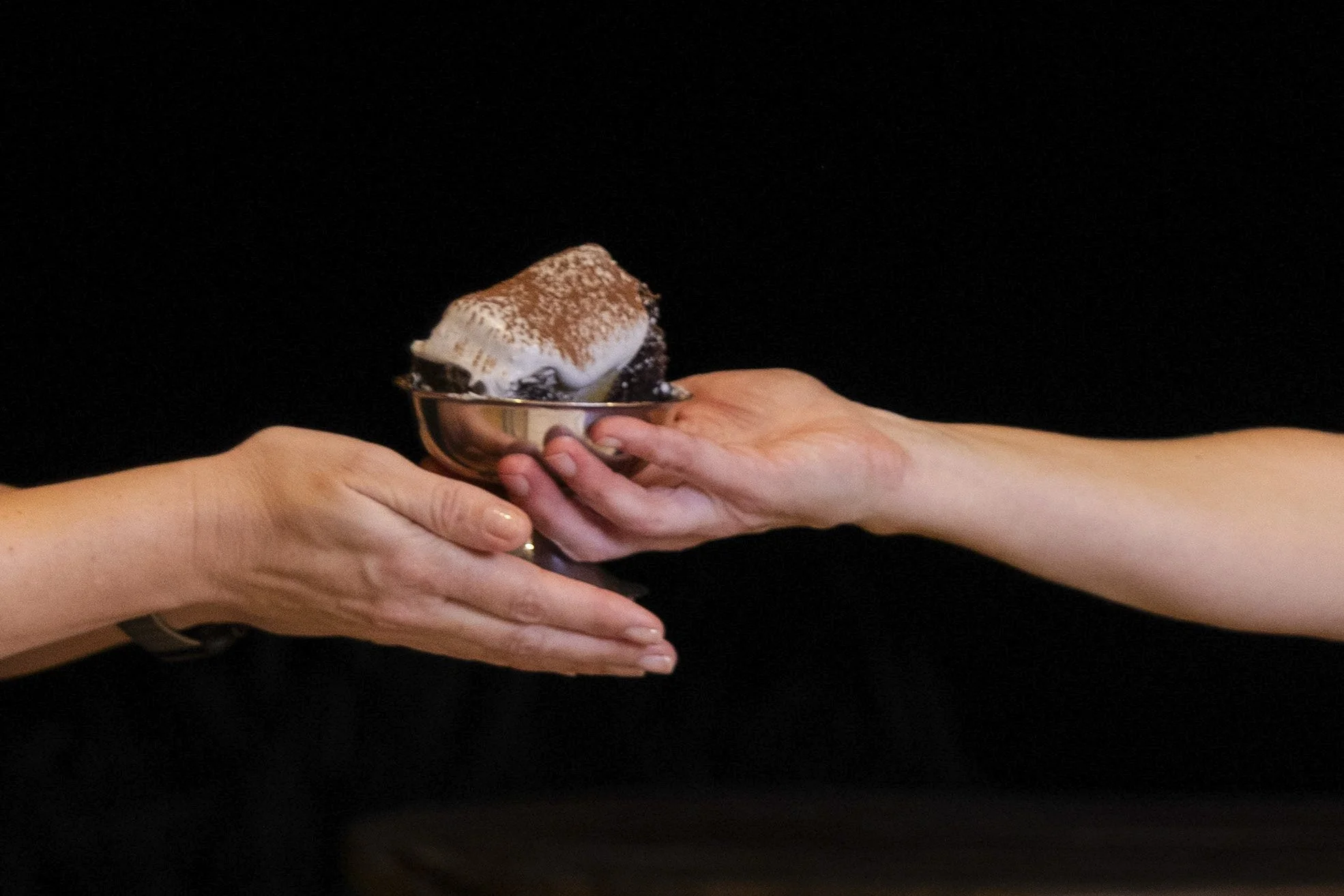 VECETO: Brutalist cake, silver bowl handover. Two hands pass a single portion across a black ground.