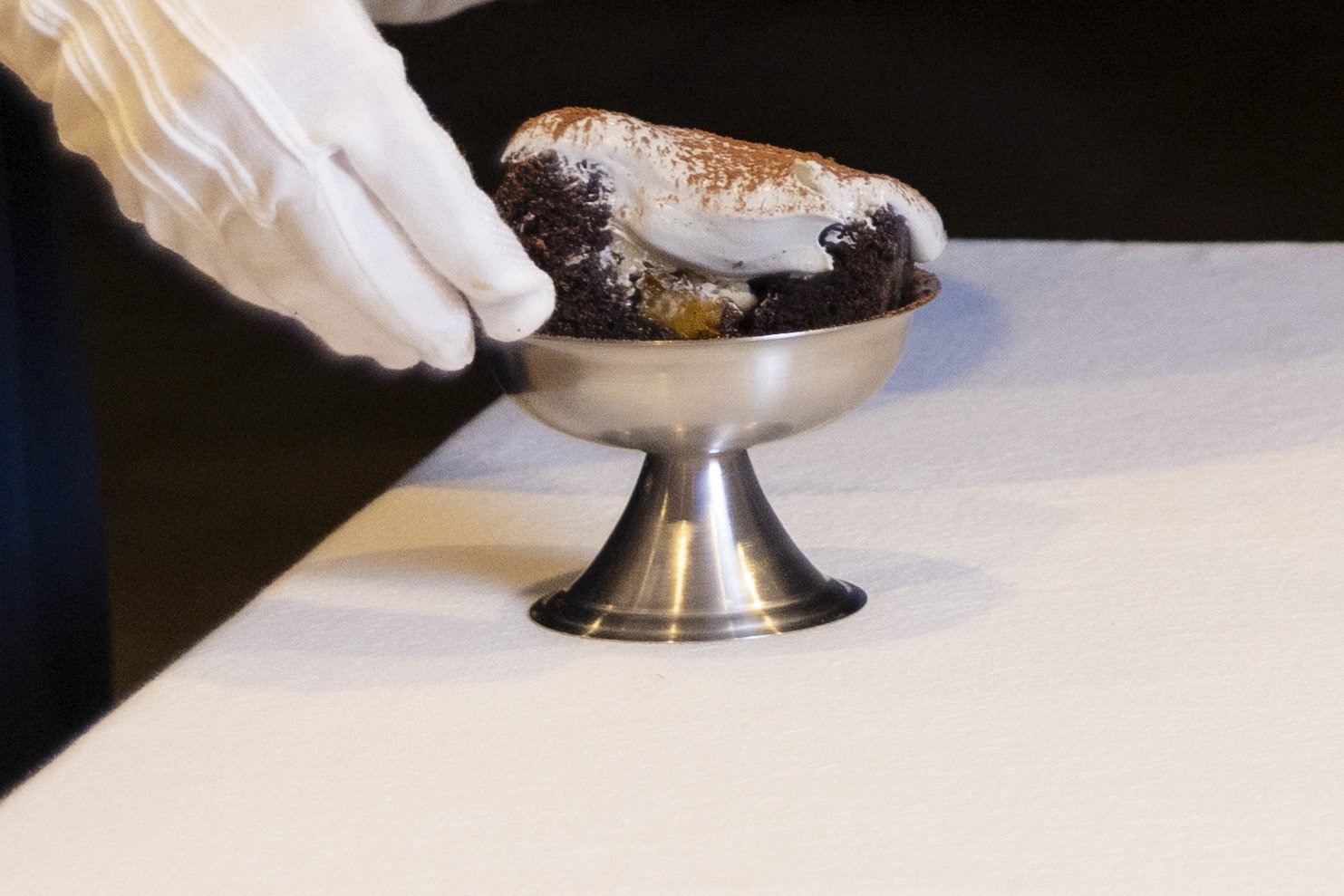 VECETO: Architectural desserts, white-gloved presentation. Gloved hand at a footed silver bowl, cut portion against the dark.