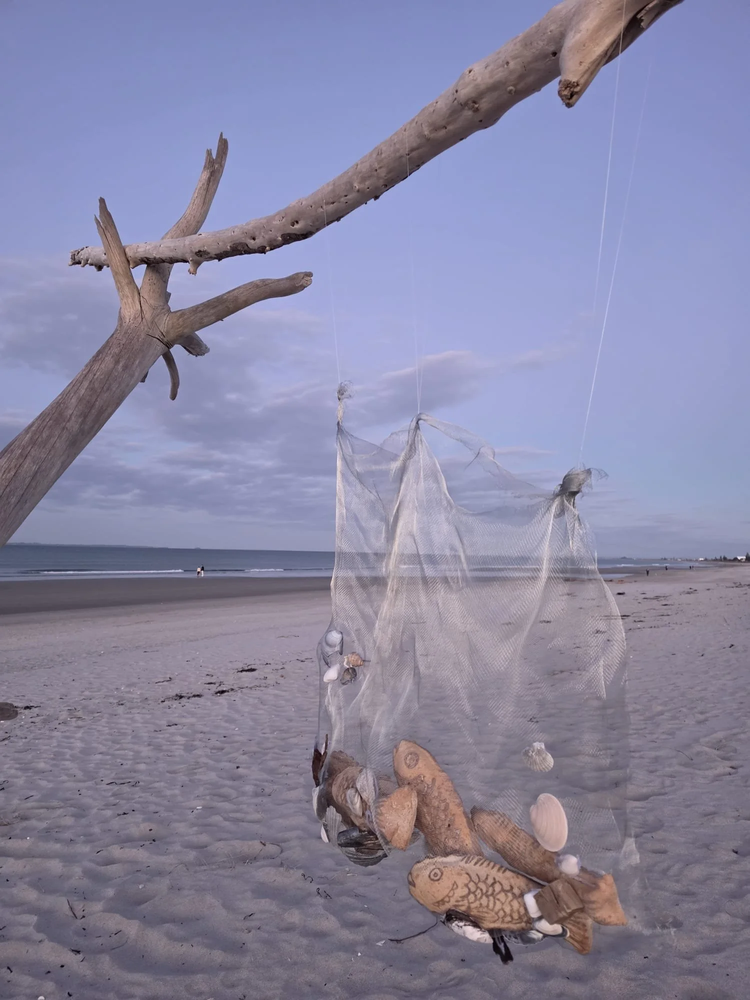 VECETO: Bread sculpture, net installation. Forked driftwood frames the net above an open, overcast shoreline.