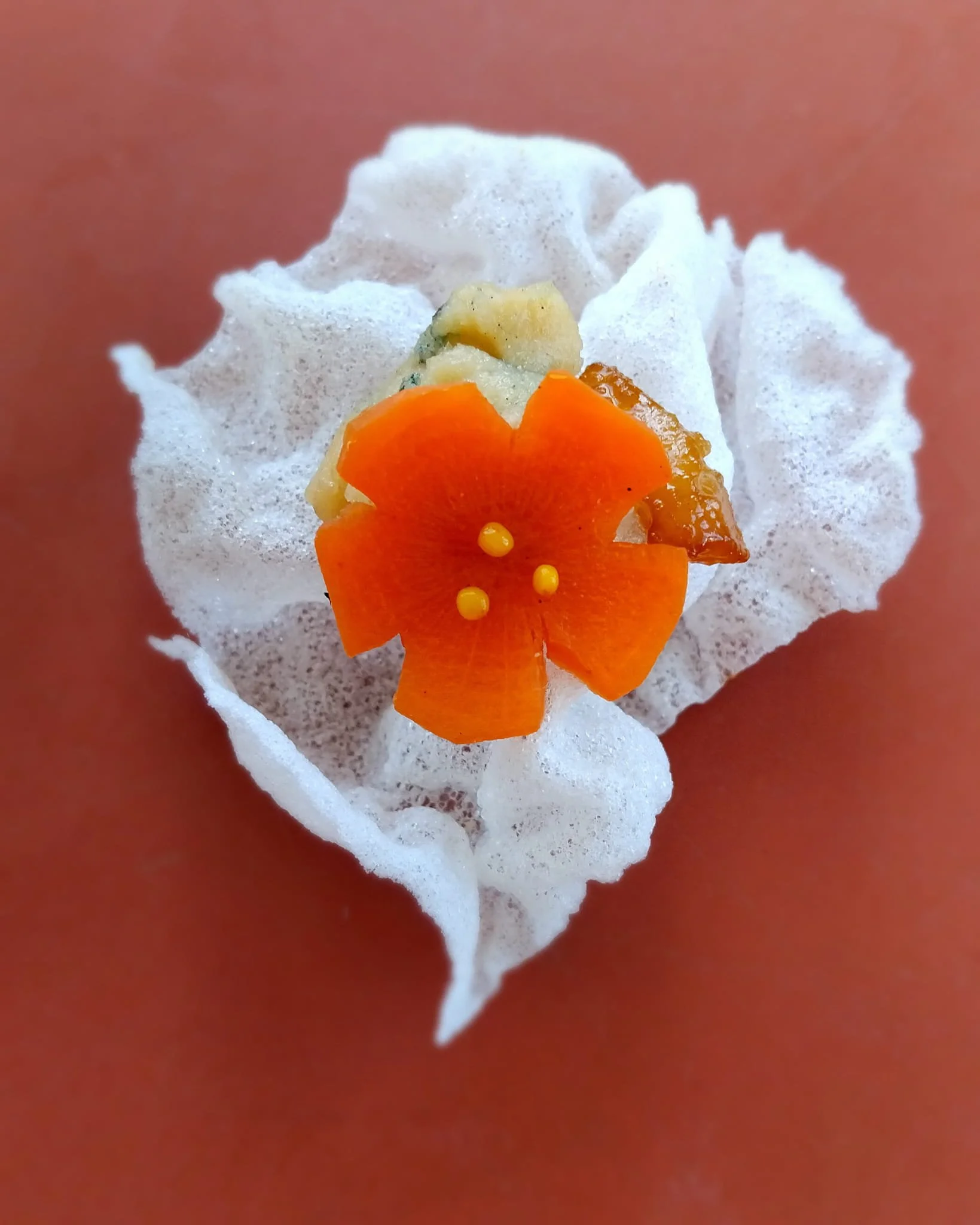 VECETO: Pickled carrot bloom on rice paper crisp, terracotta behind. Culinary art direction.