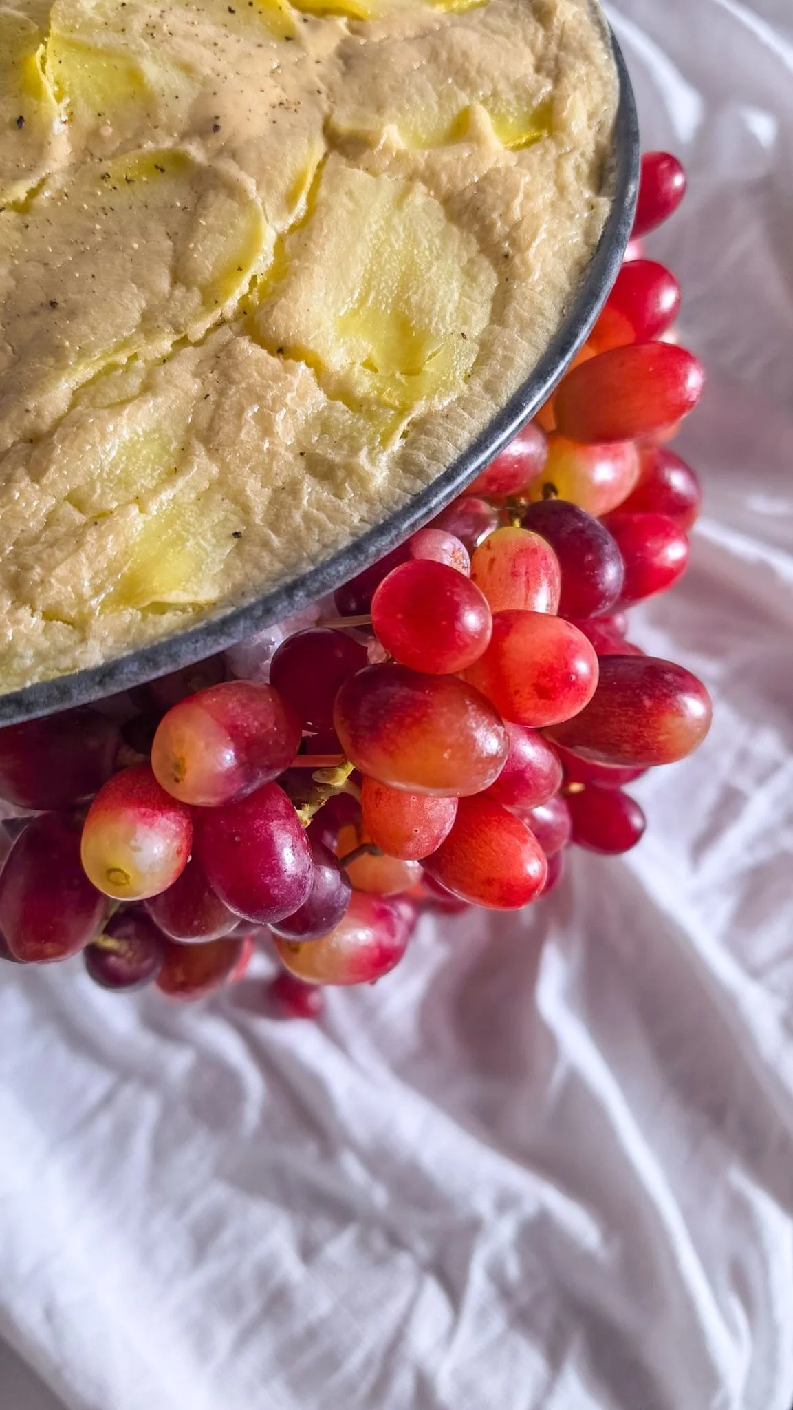 VECETO: Cashew cream over potato gratin, pink grapes at the rim below. Tactile materiality, classical grey
