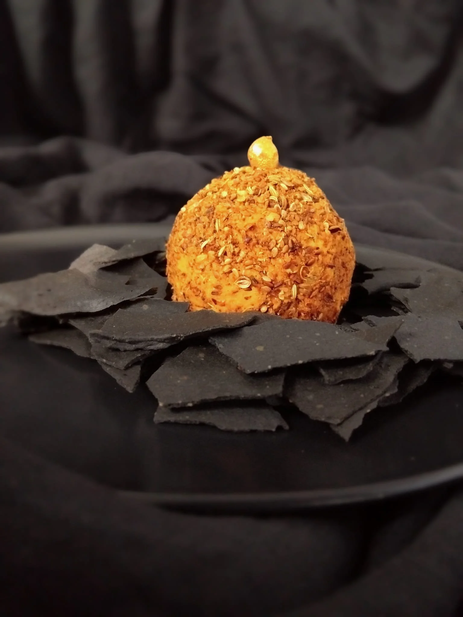 VECETO: Charcoal crackers set in rows around pumpkin hummus in dukkah, gold hazelnut at the centre. Spatial composition.