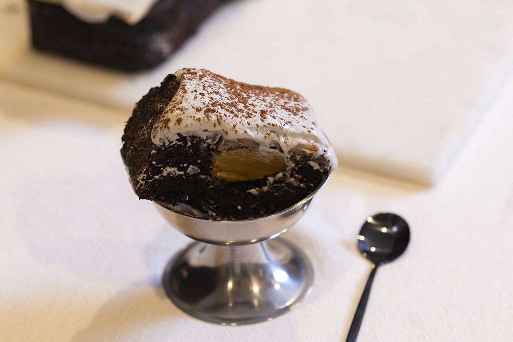 VECETO: Architectural desserts, brutalist cake cut in section. One portion in a footed silver bowl, black spoon beside.