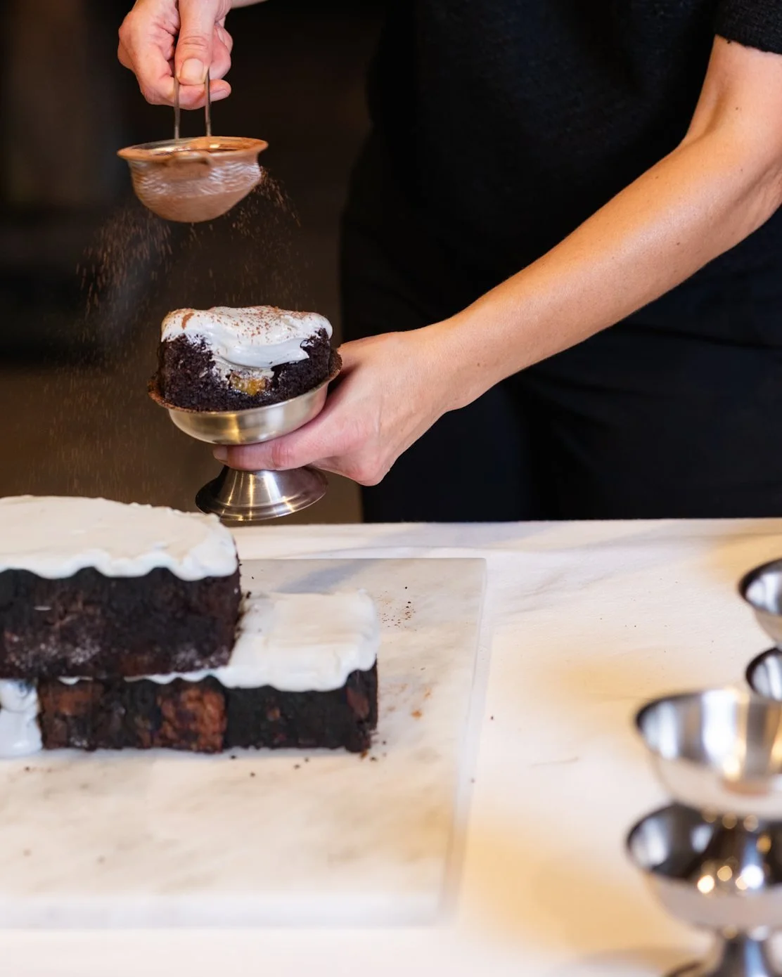 VECETO: Brutalist cake, partly dismantled. Cacao sifted over one portion in silver, the opened wall behind.