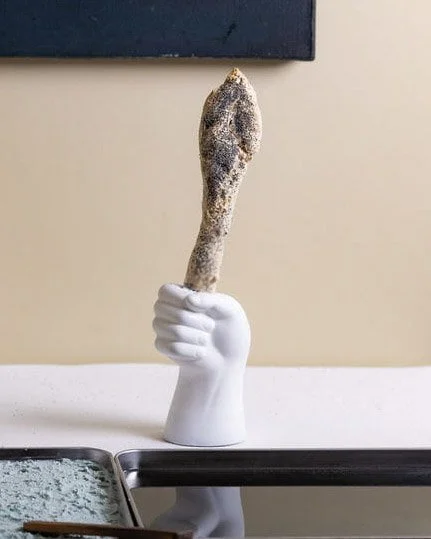 VECETO: Food performance art, durational tableau. Bread sceptre rises from a ceramic hand vessel beside navy spirulina oil.