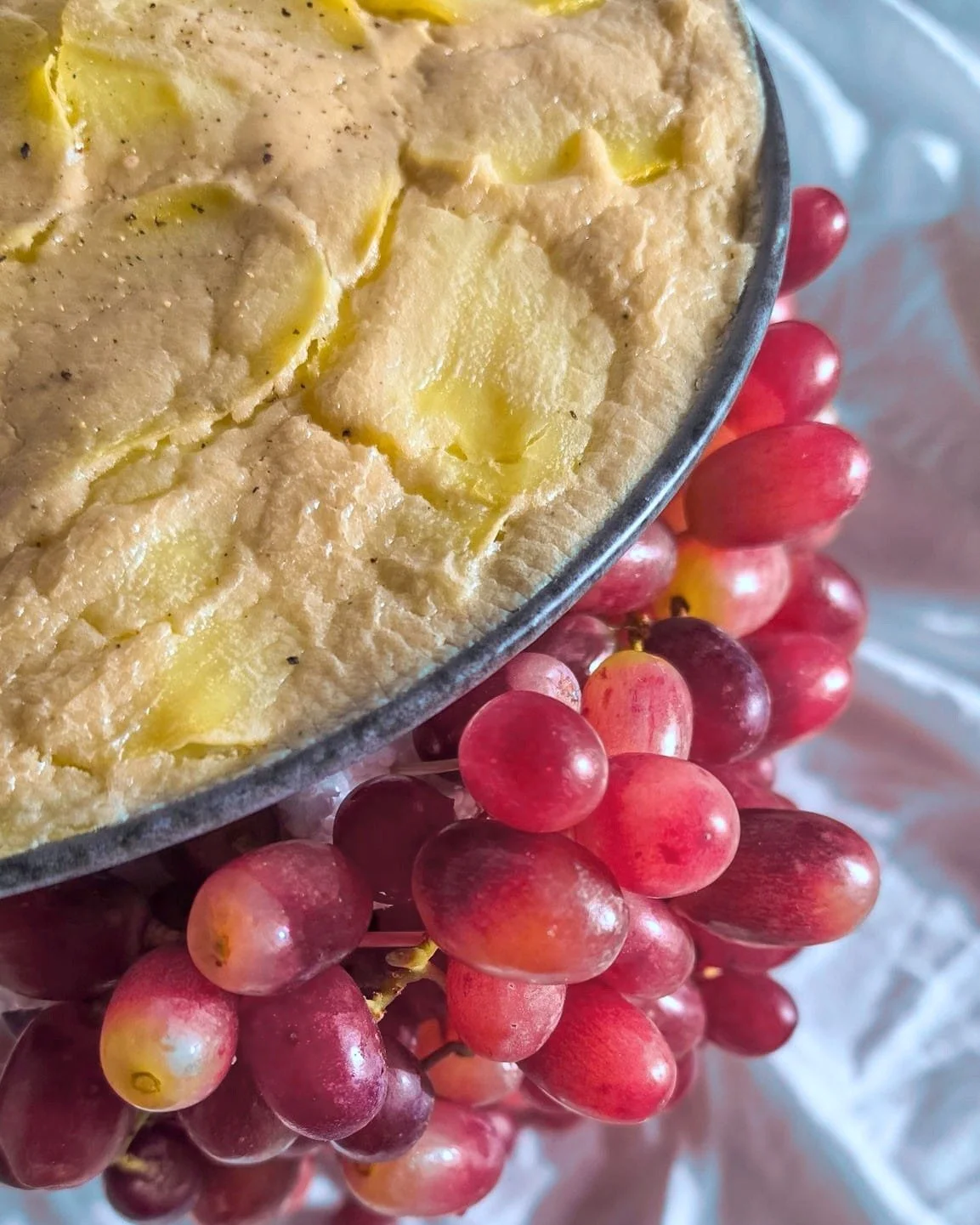 VECETO: Conceptual food art, gratin in a dark grey bowl seen from above, pink grapes gathered at the rim.