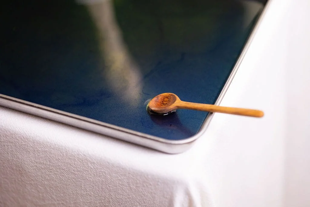 VECETO: Durational tableau. A ceramic hand reflects in navy spirulina oil beneath a bread sceptre.