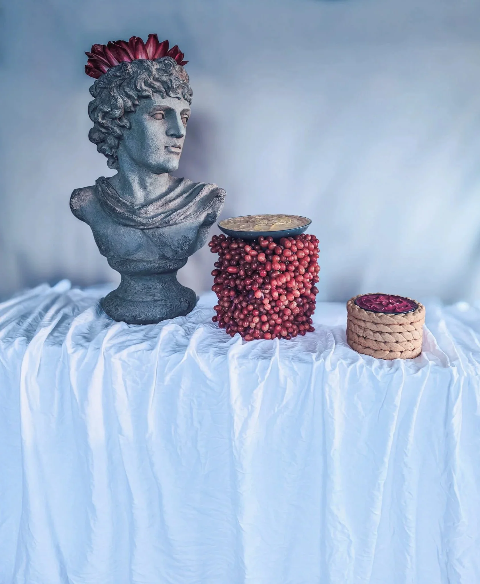 VECETO: Bust, grape column and bread rings at halving heights. Site-specific installation art, classical grey.