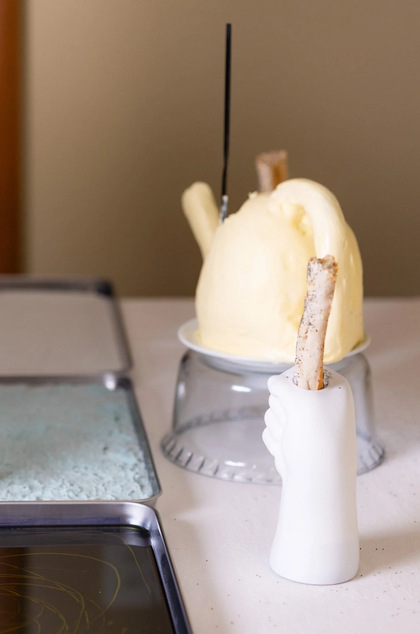 VECETO: Material transformation, food performance art. Butter watering can sculpture beside a triptych of blue trays.