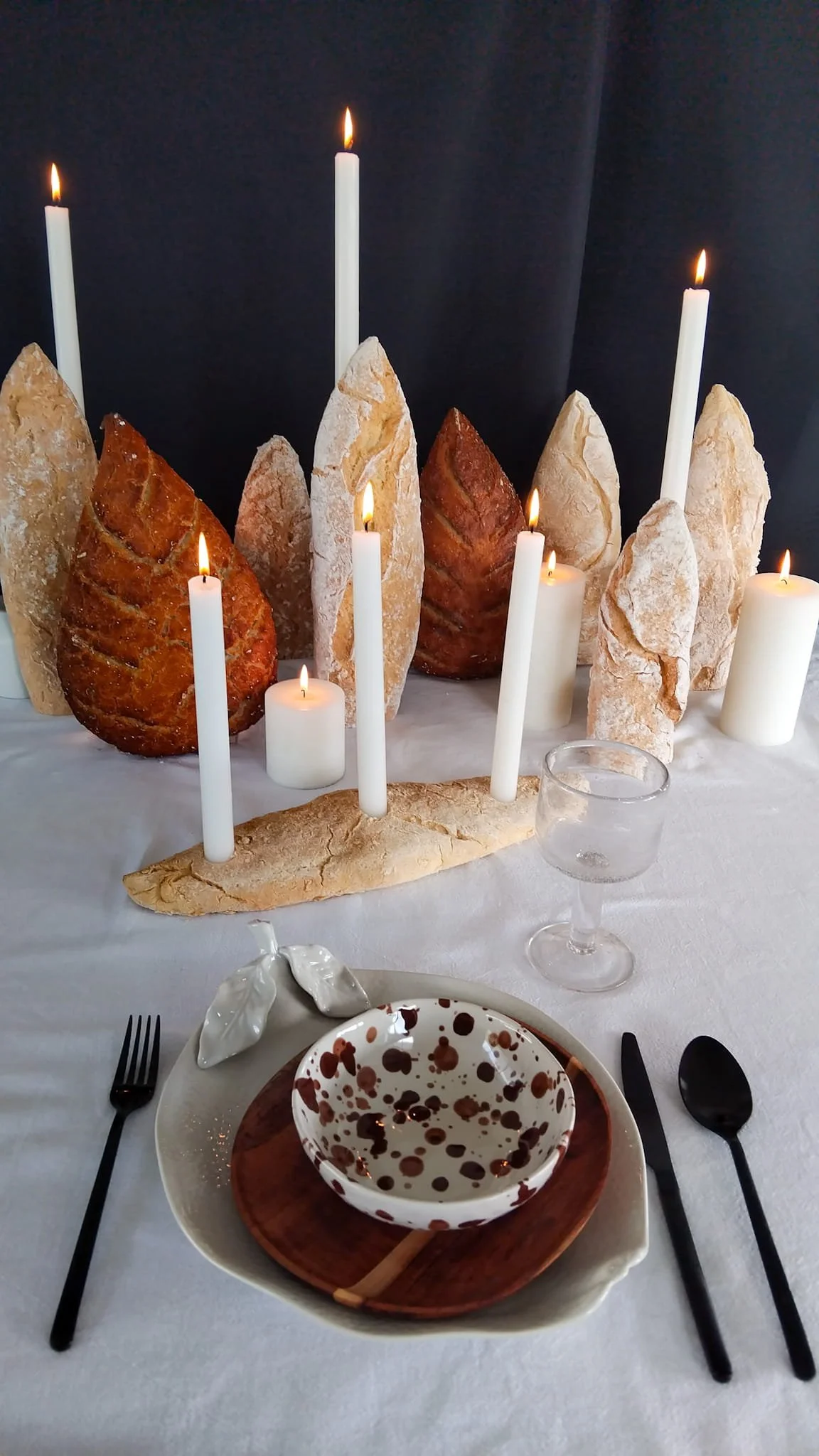 Radical elegance. Vertical bread sculptures and glowing candles on a white tablecloth against black backdrop.