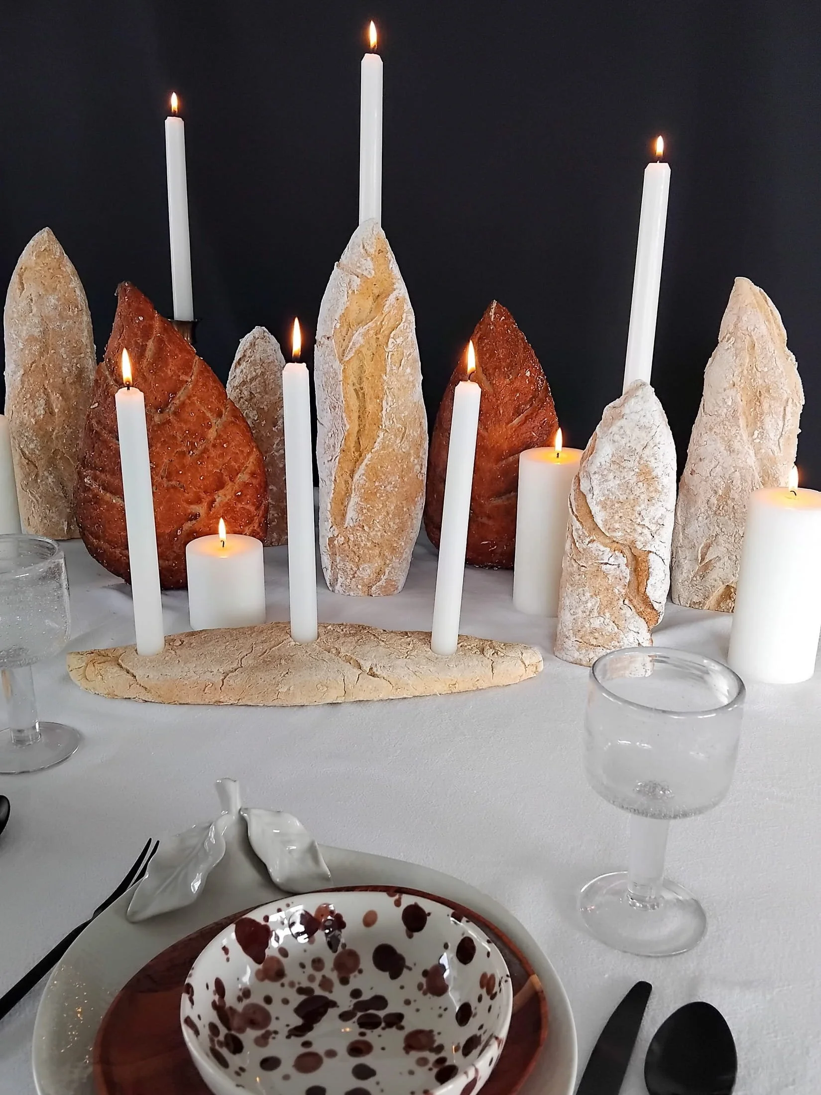 VECETO: Standing sourdough and ciabatta among lit block candles, dark ground. Foodscape.