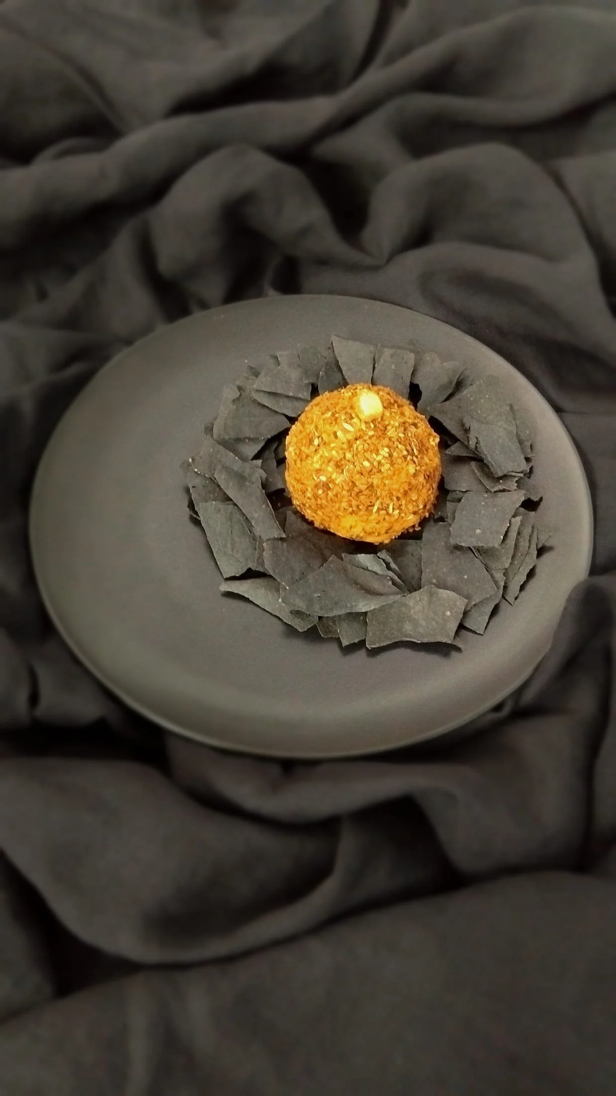 VECETO: Charcoal cracker seen from a high angle, plate centred in a vertical frame, black throughout.
