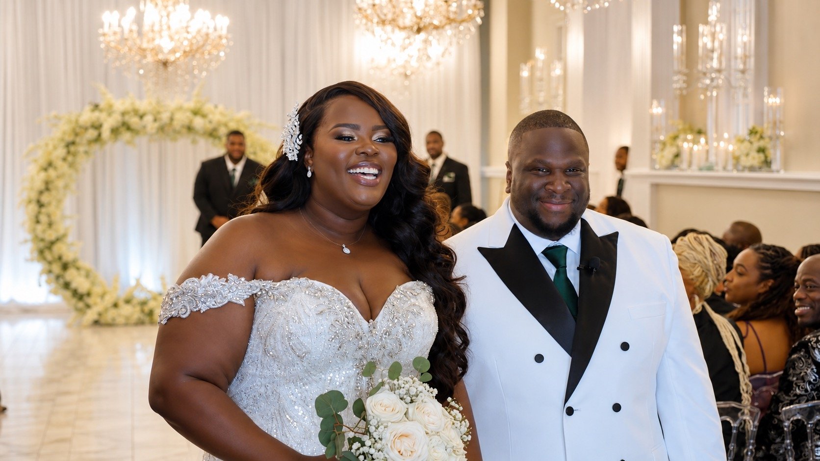 A bride and groom smiling at their wedding ceremony, with wedding guests and floral decorations in the background.