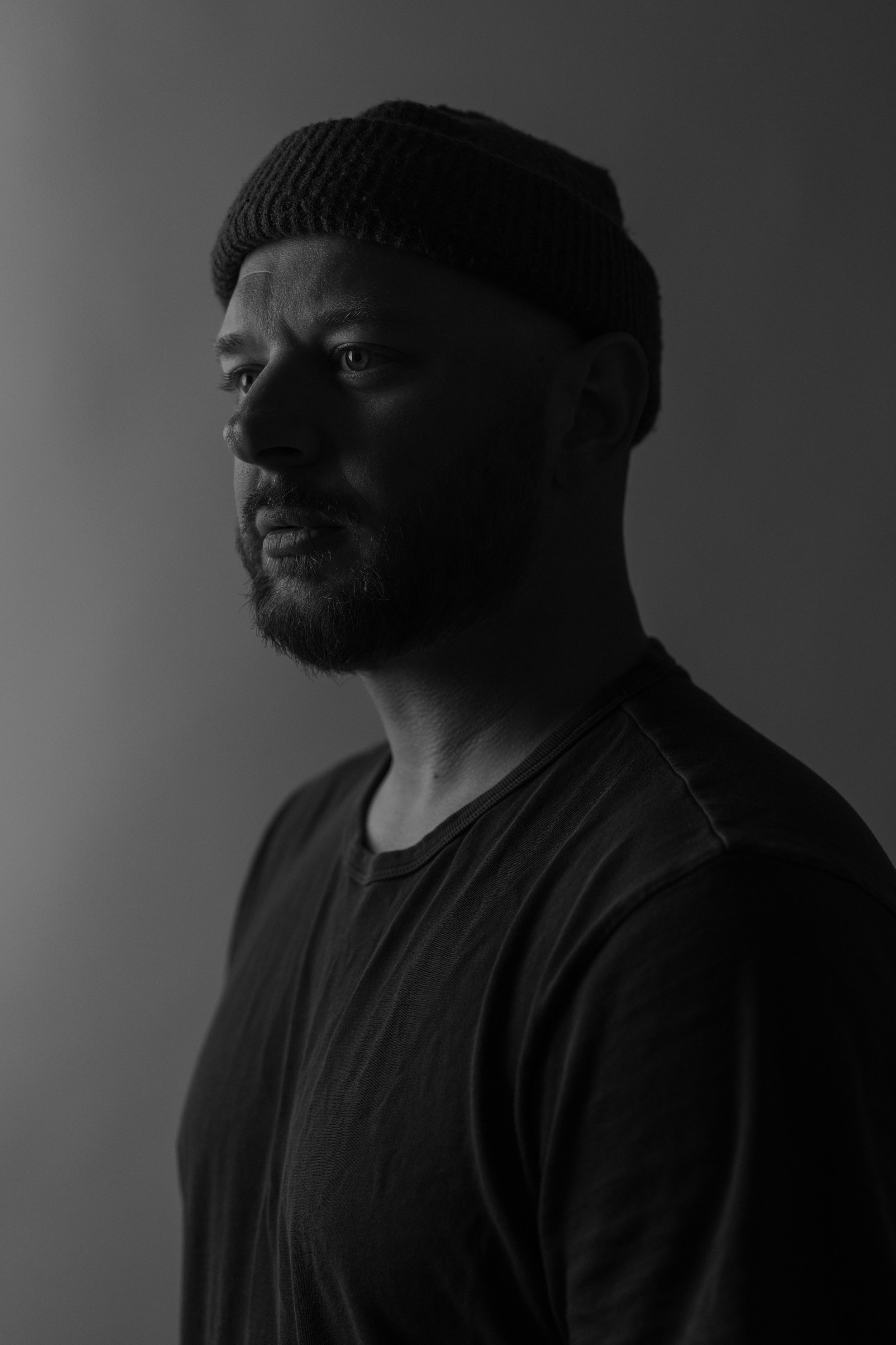 Black and white portrait of a man wearing a beanie, gazing to the side, in a thoughtful expression.