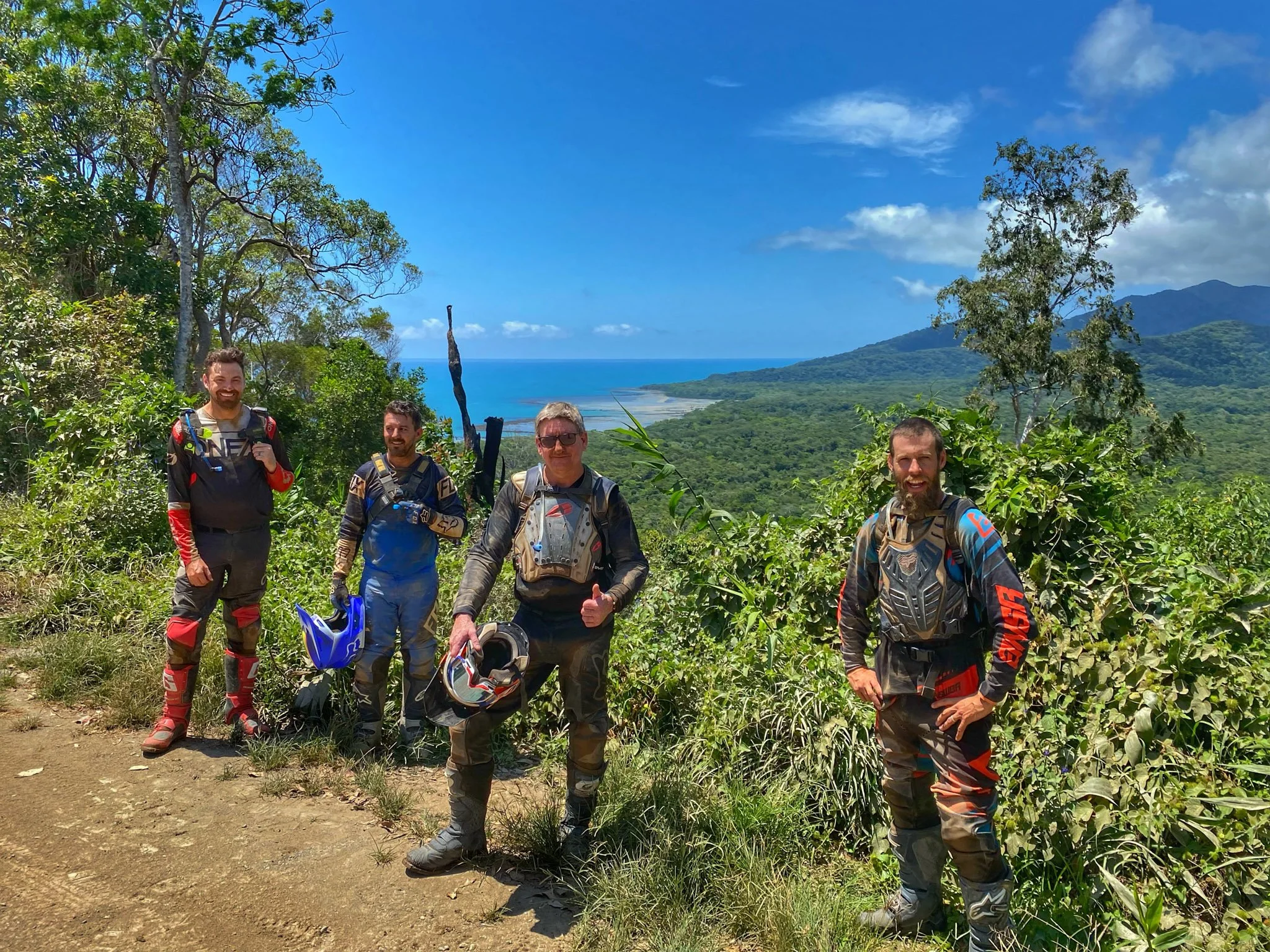 Group of riders on a Cairns motorcycle tour standing at a coastal lookout overlooking rainforest and ocean near the Daintree in Far North Queensland